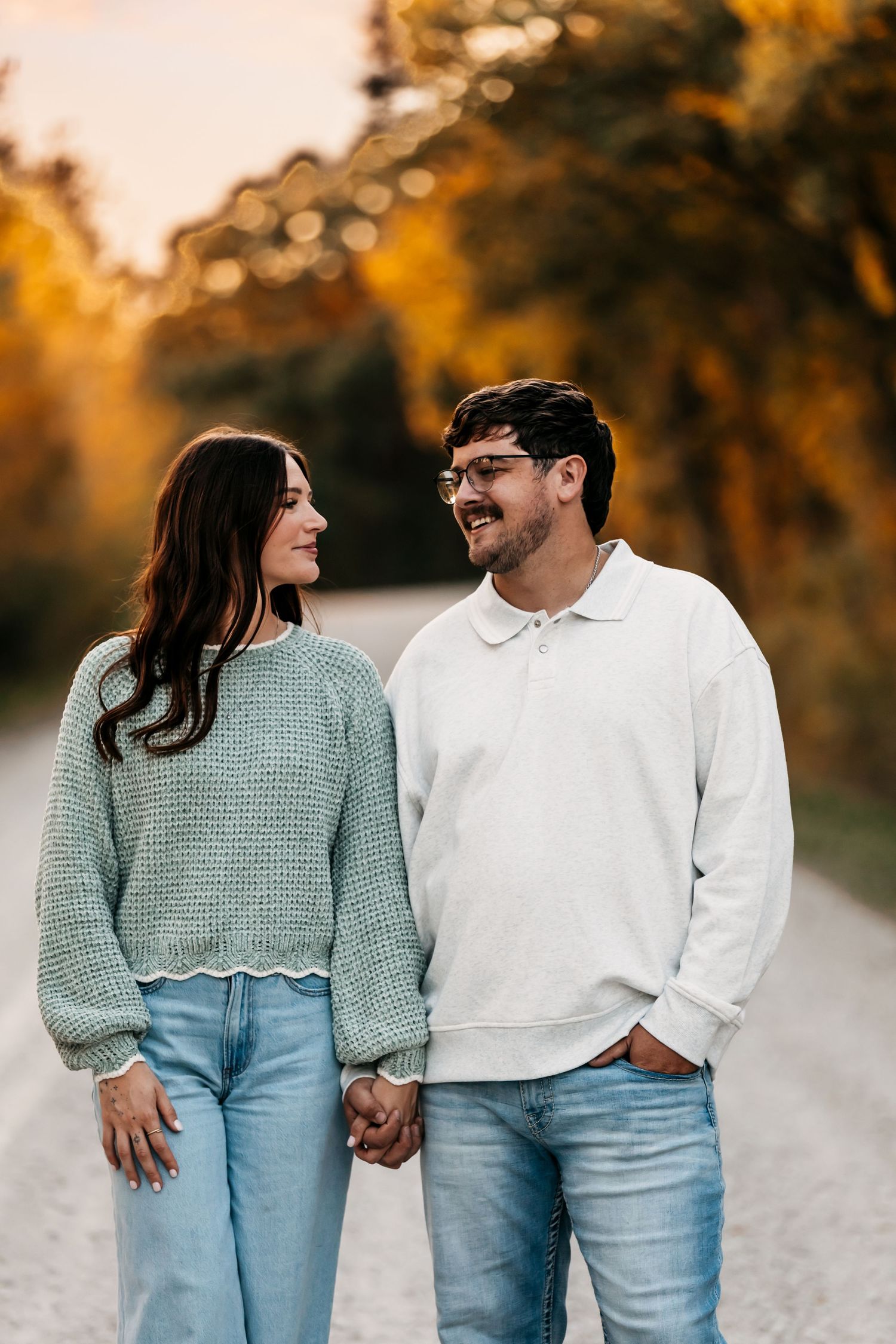 Couple in matching casual wear smiling at each other on a country road during golden hour.