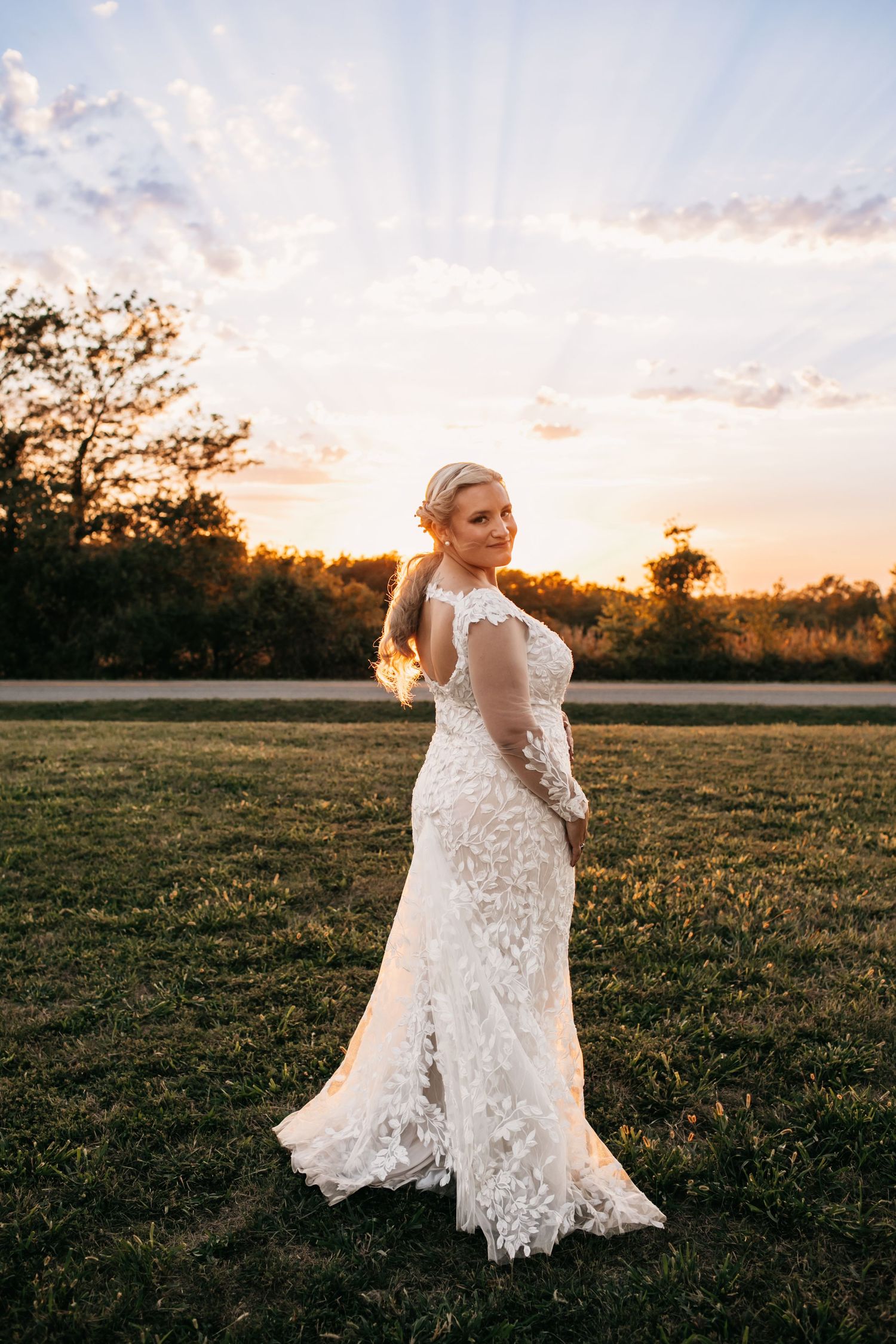 Lace wedding dress flowing in golden sunset light across a field.