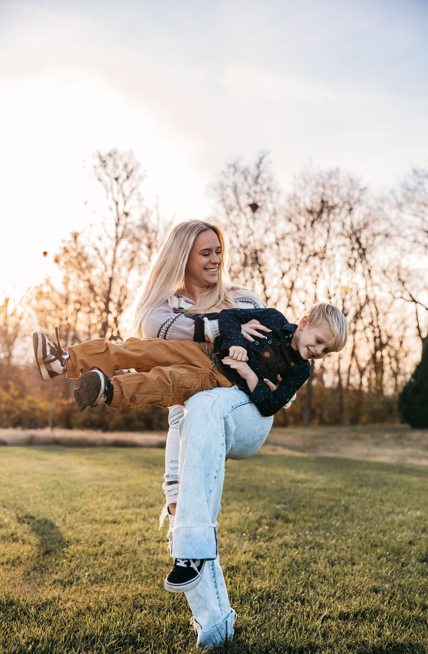 Parent and child playing and laughing together in outdoor field at sunset.