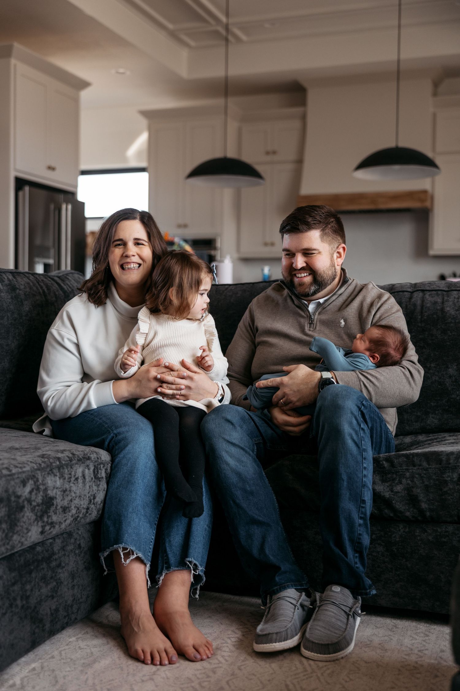 Family sharing intimate moments and laughter while sitting together on dark gray couch.