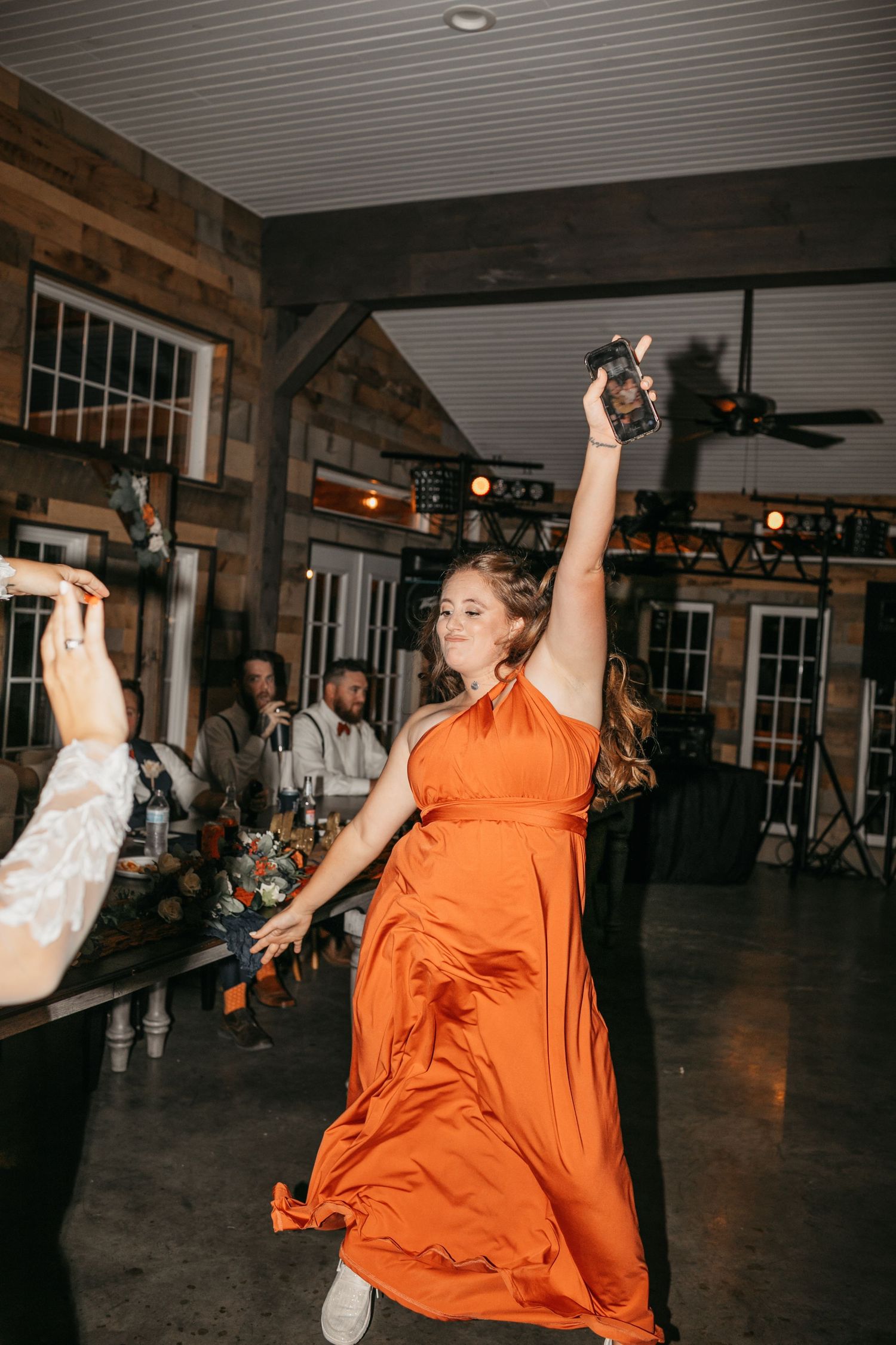 Energetic dancing at a wedding reception with bright orange attire.