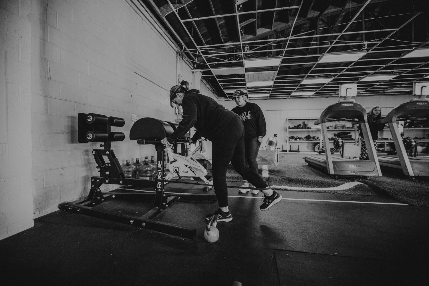 Industrial gym space with exposed ceiling and fitness equipment lined against white walls.