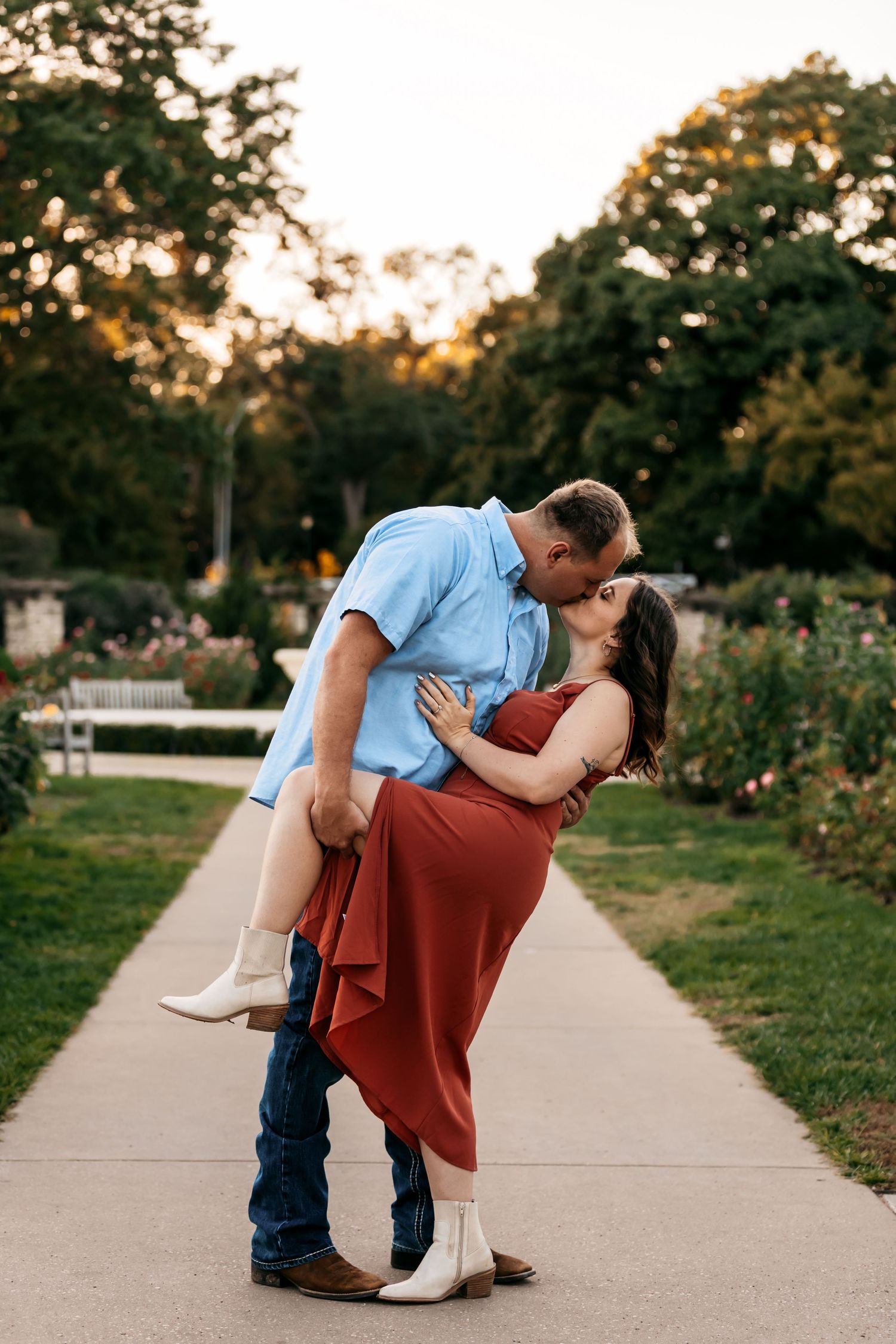 A couple performs a romantic dip pose on a garden pathway at sunset.