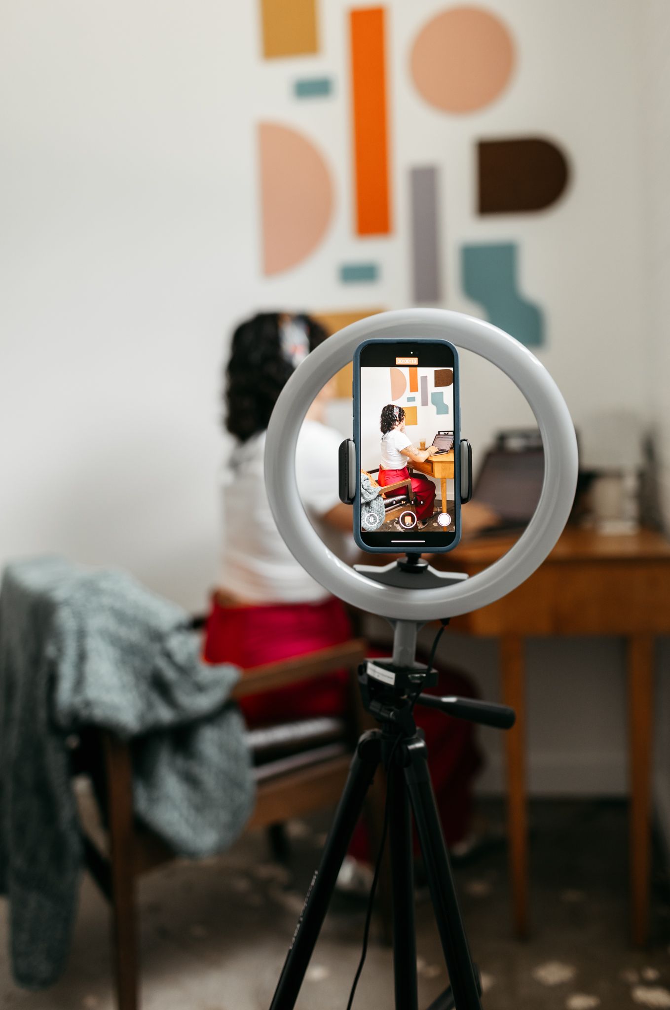 Ring light setup with phone camera capturing content against abstract wall art.