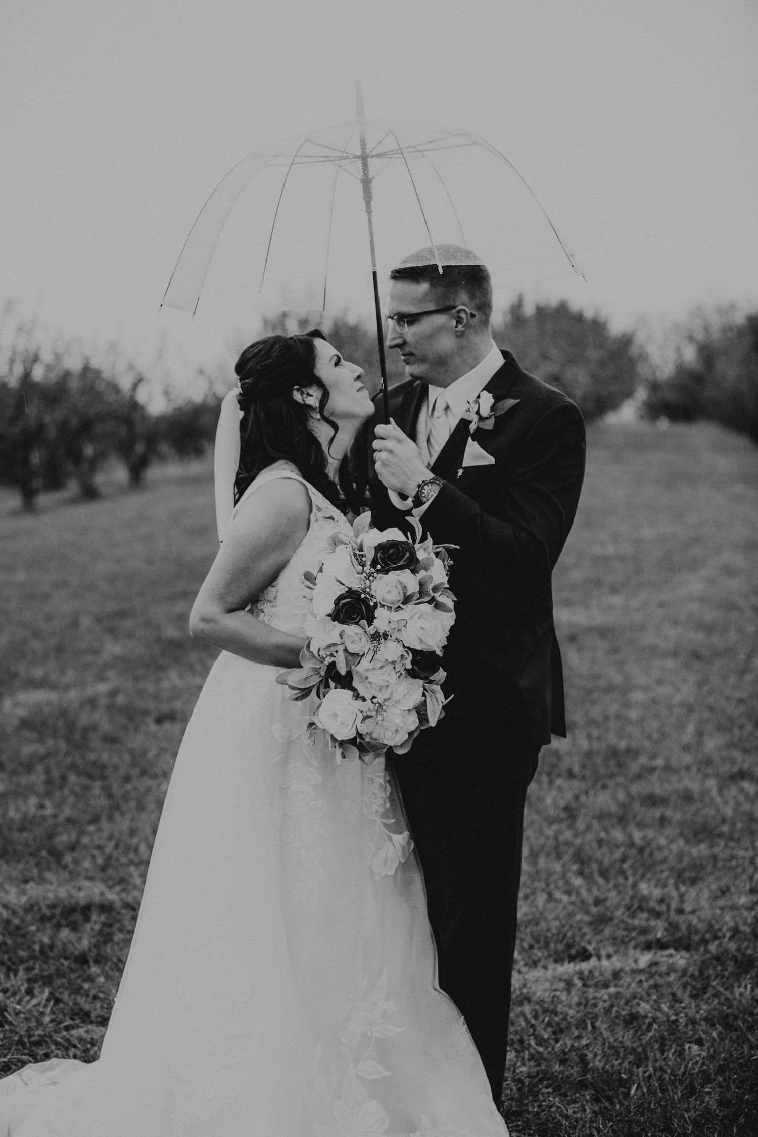 A romantic moment captured in black and white with a couple sharing an umbrella in a field.