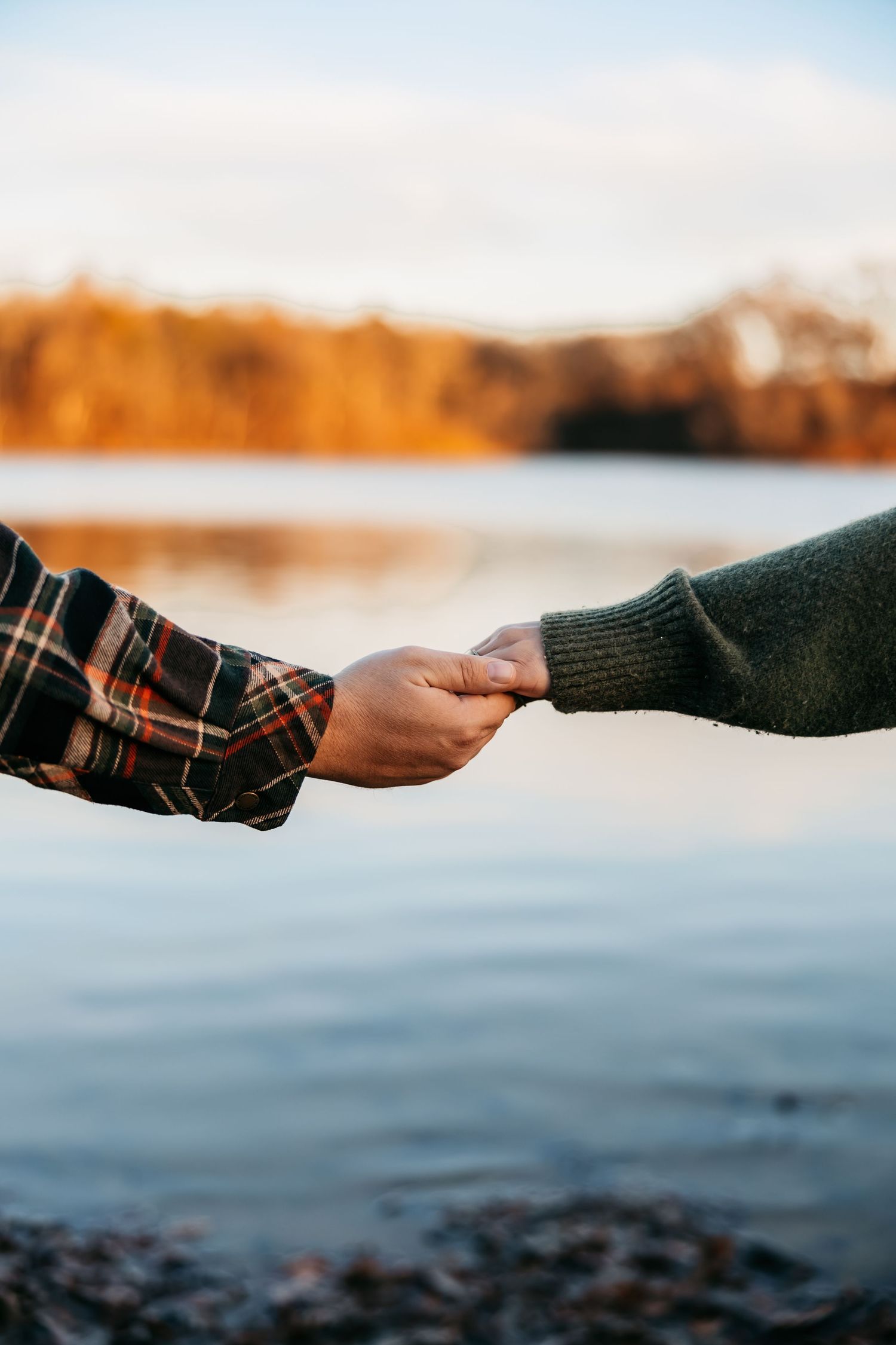Two hands reach out to touch across a serene waterfront backdrop at sunset.