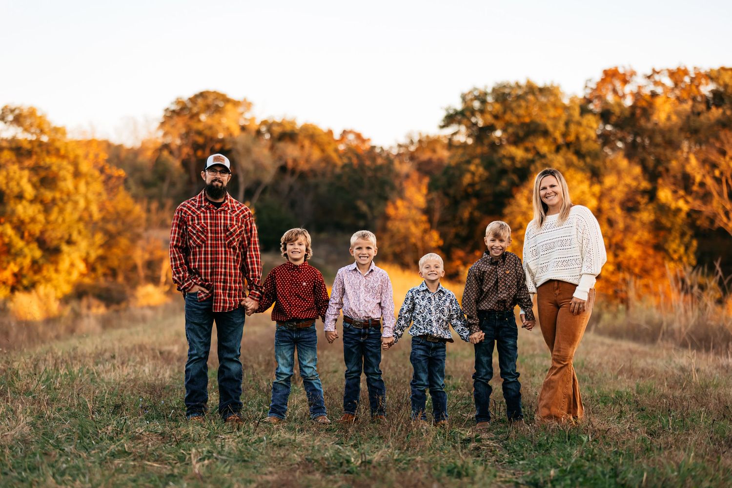 A family of 6 lined up on a grassy hill against a warm autumn sunset backdrop in Missouri.