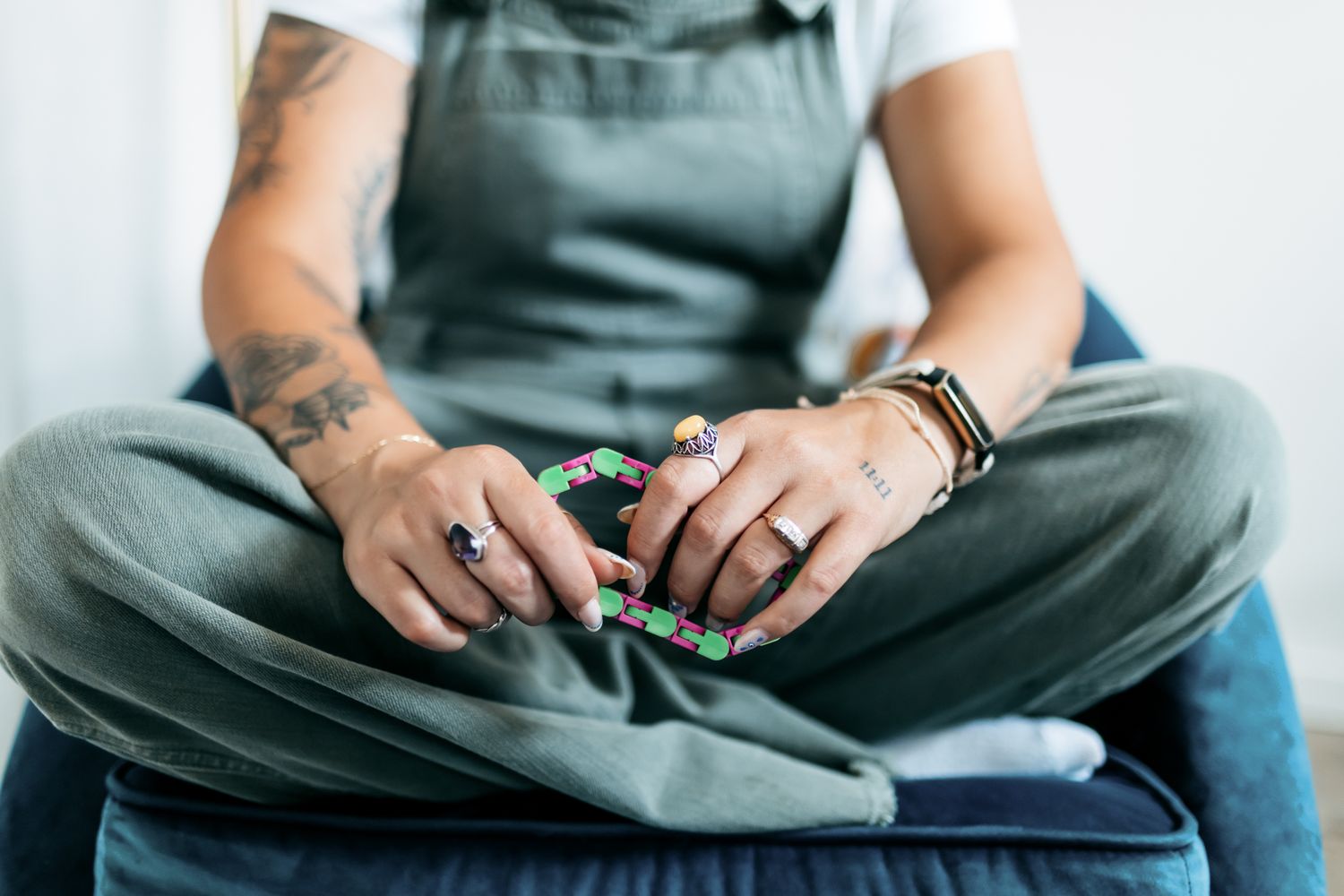 Detail shot of hands with rings and tattoos resting on green fabric.