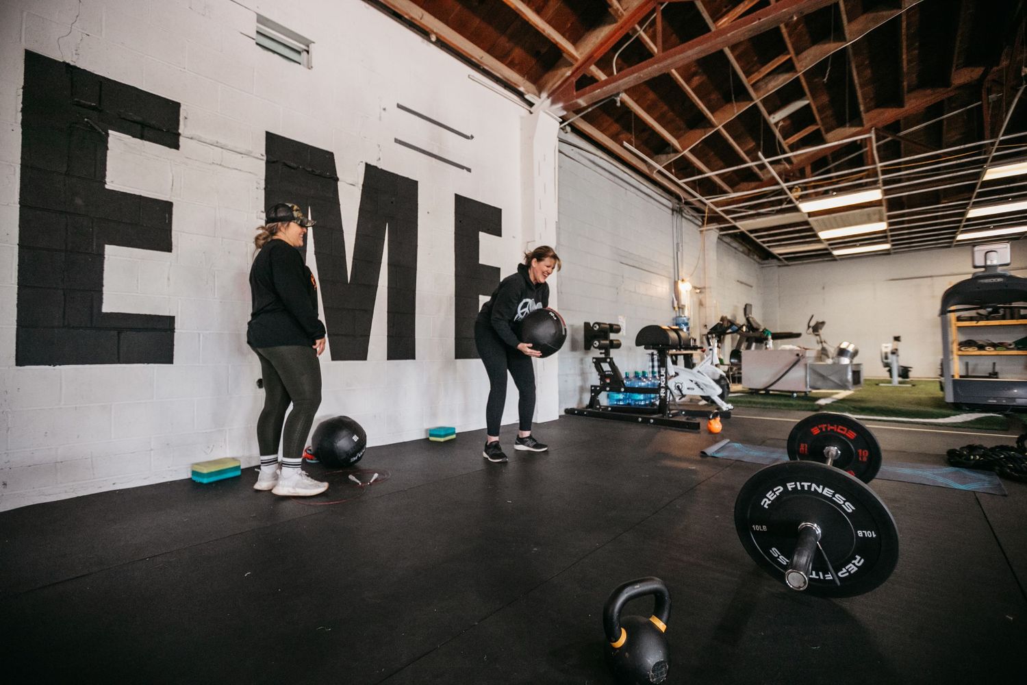 Panoramic view of a modern gym facility with white walls and exposed ceiling beams.