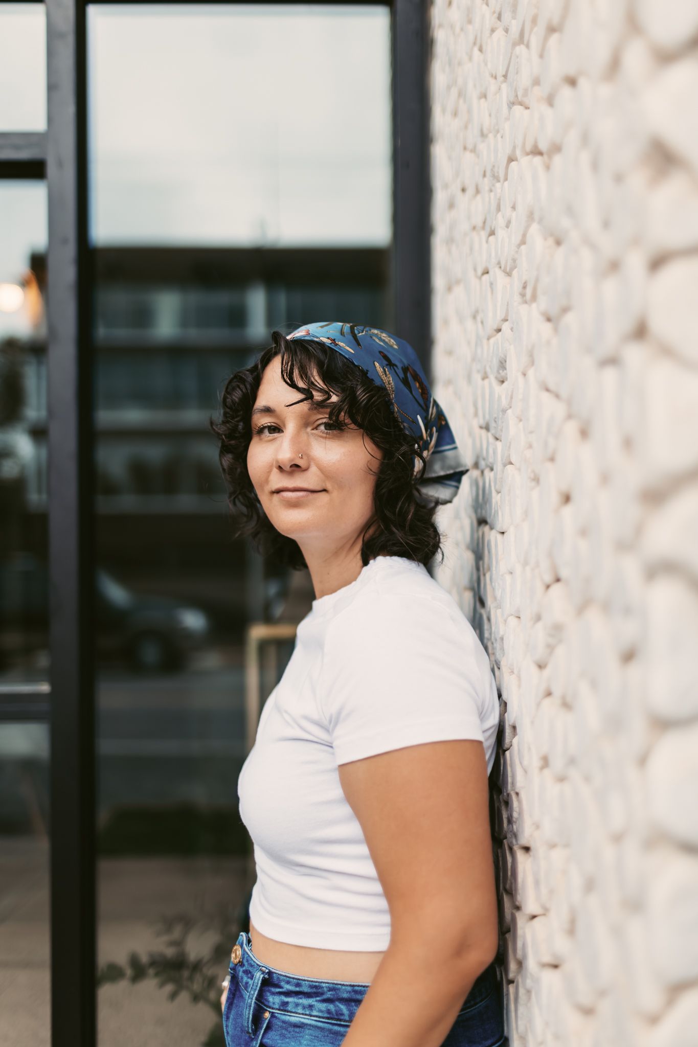 Lifestyle portrait against a textured wall wearing a white crop top and blue denim.
