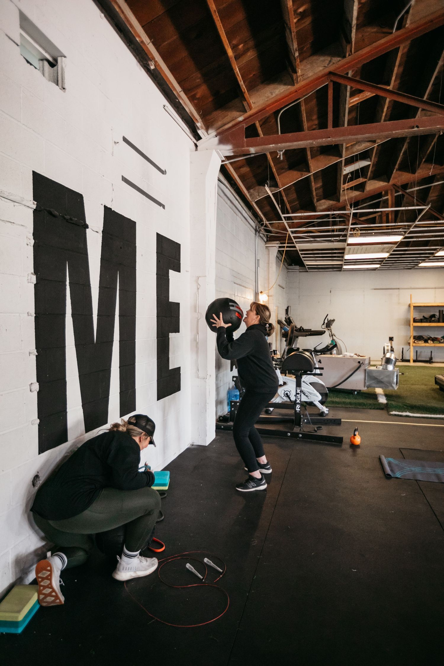 Fitness enthusiasts working out in an industrial-style gym with ME text on white walls.