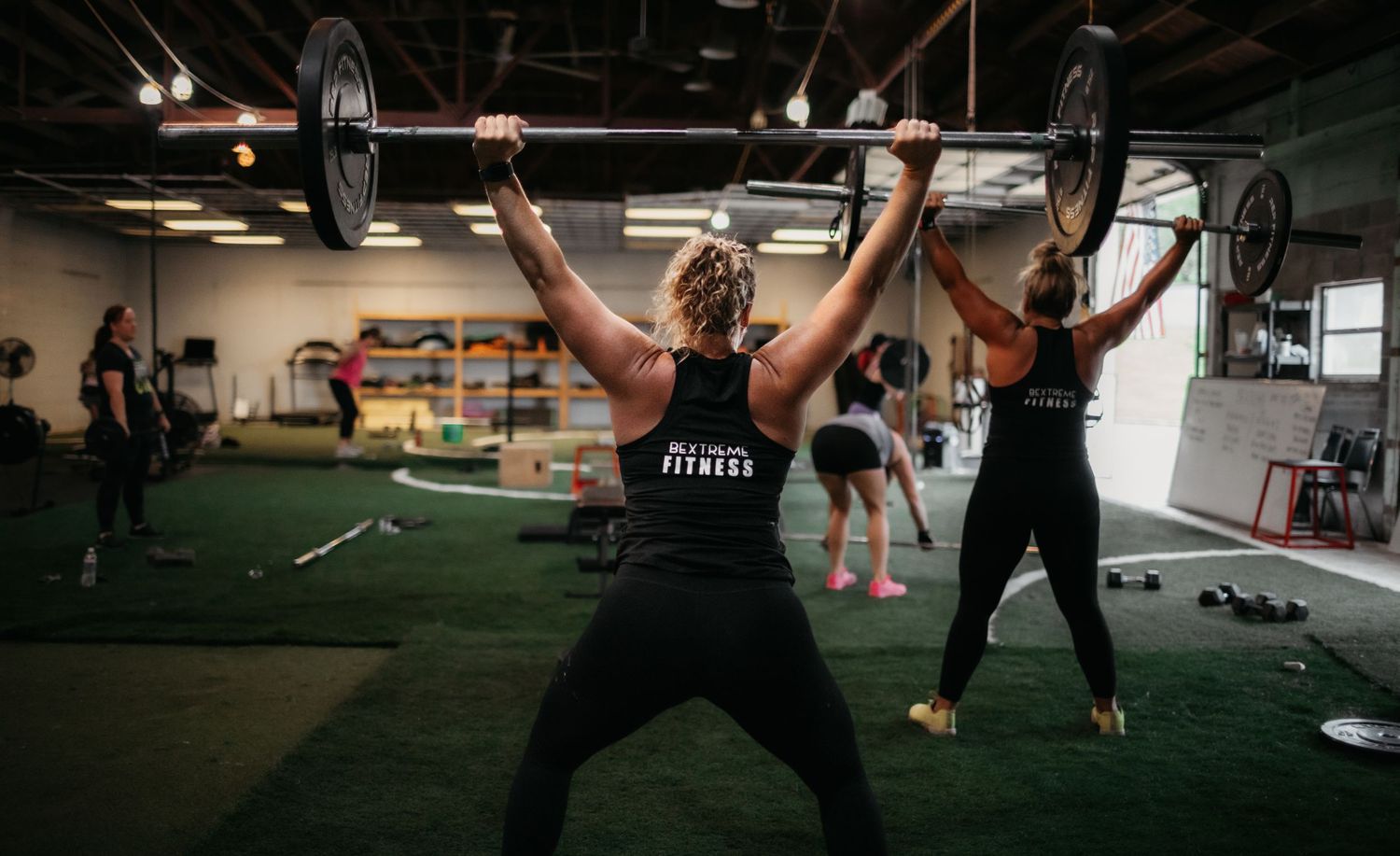Athletes lifting weights during a group training session in an industrial gym space.