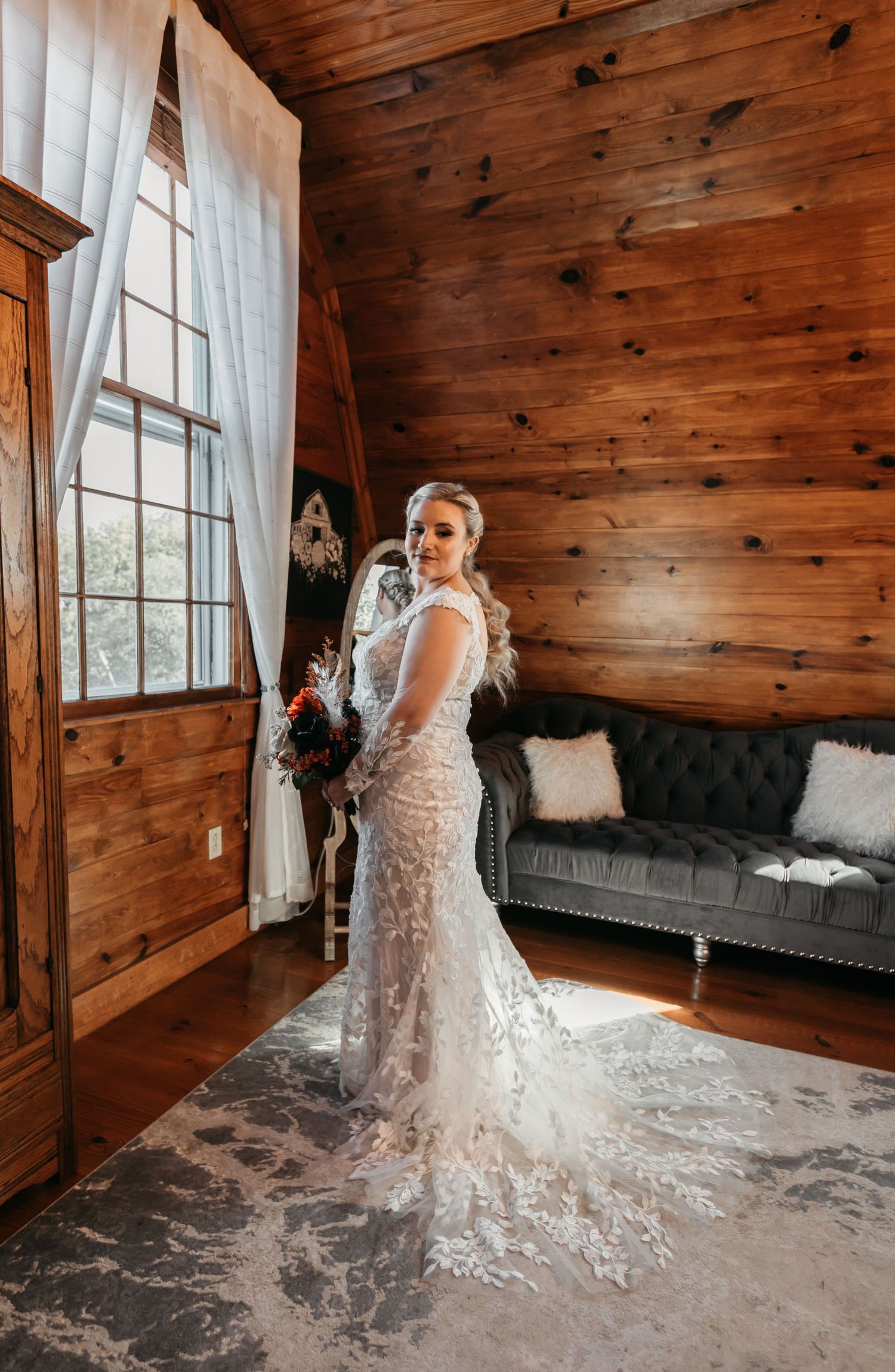 Elegant lace wedding dress photographed in rustic cabin with wooden walls and natural light.