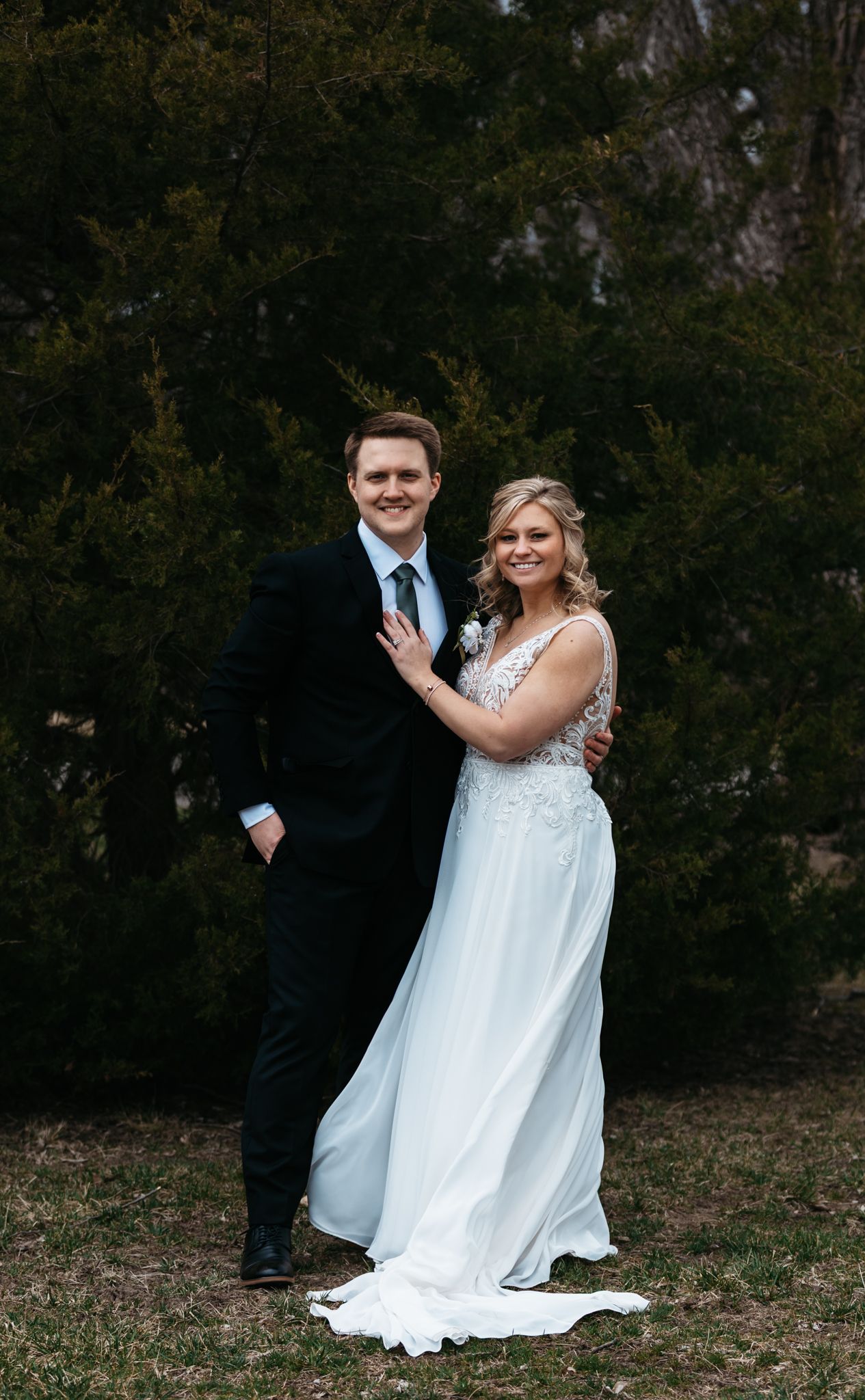 Wedding couple poses playfully outside in formal attire against natural backdrop.