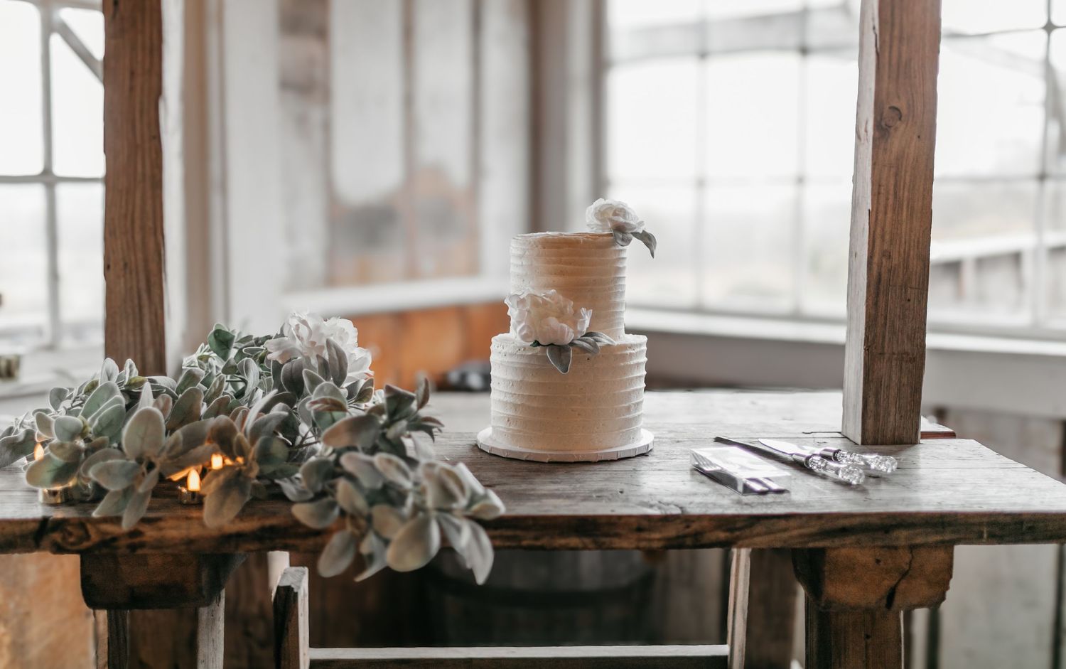 Elegant wedding cake display with eucalyptus decorations on wooden rustic tables.
