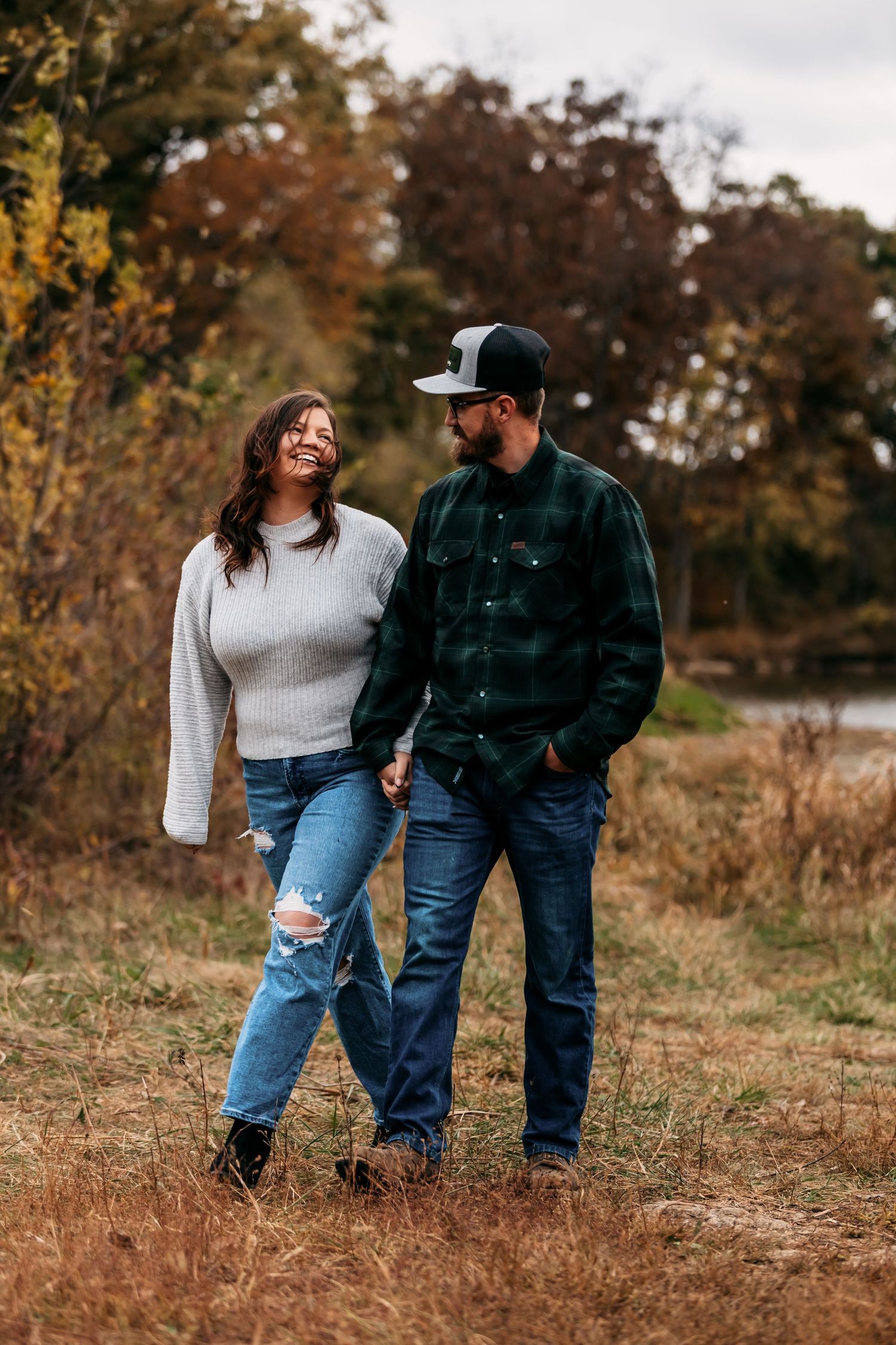 A couple takes a stroll through an autumn field wearing coordinating casual outfits.