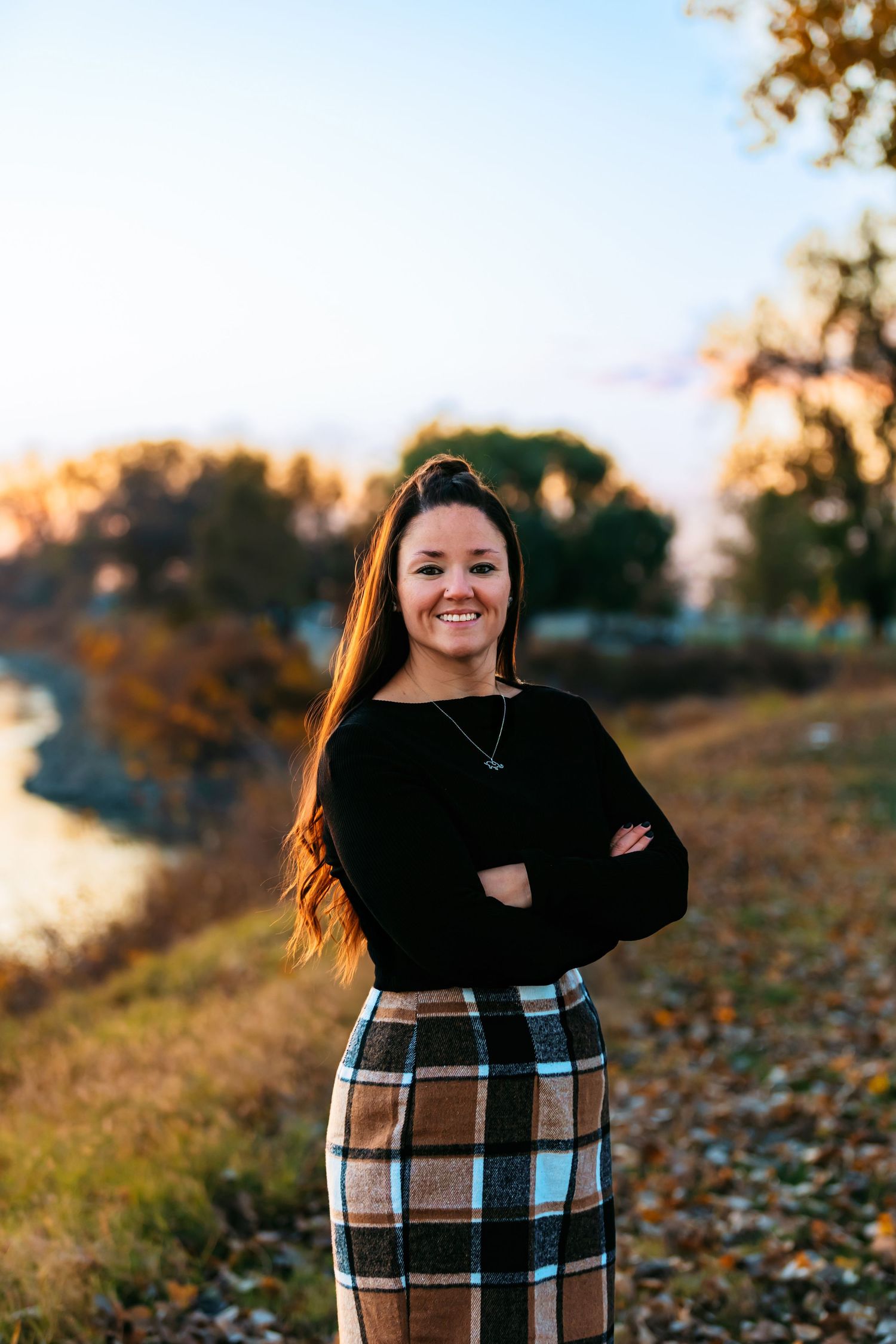 Autumn outdoor portrait in a plaid skirt and black sweater with fall foliage in background.