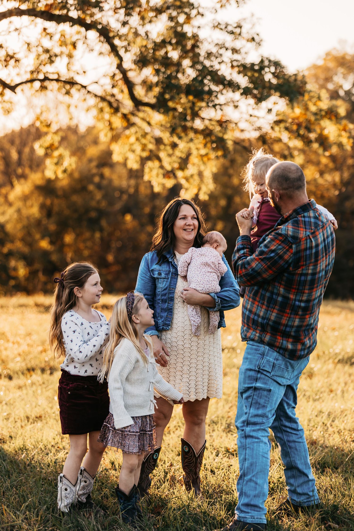 Family playing and dancing together in a sunlit meadow during golden hour.