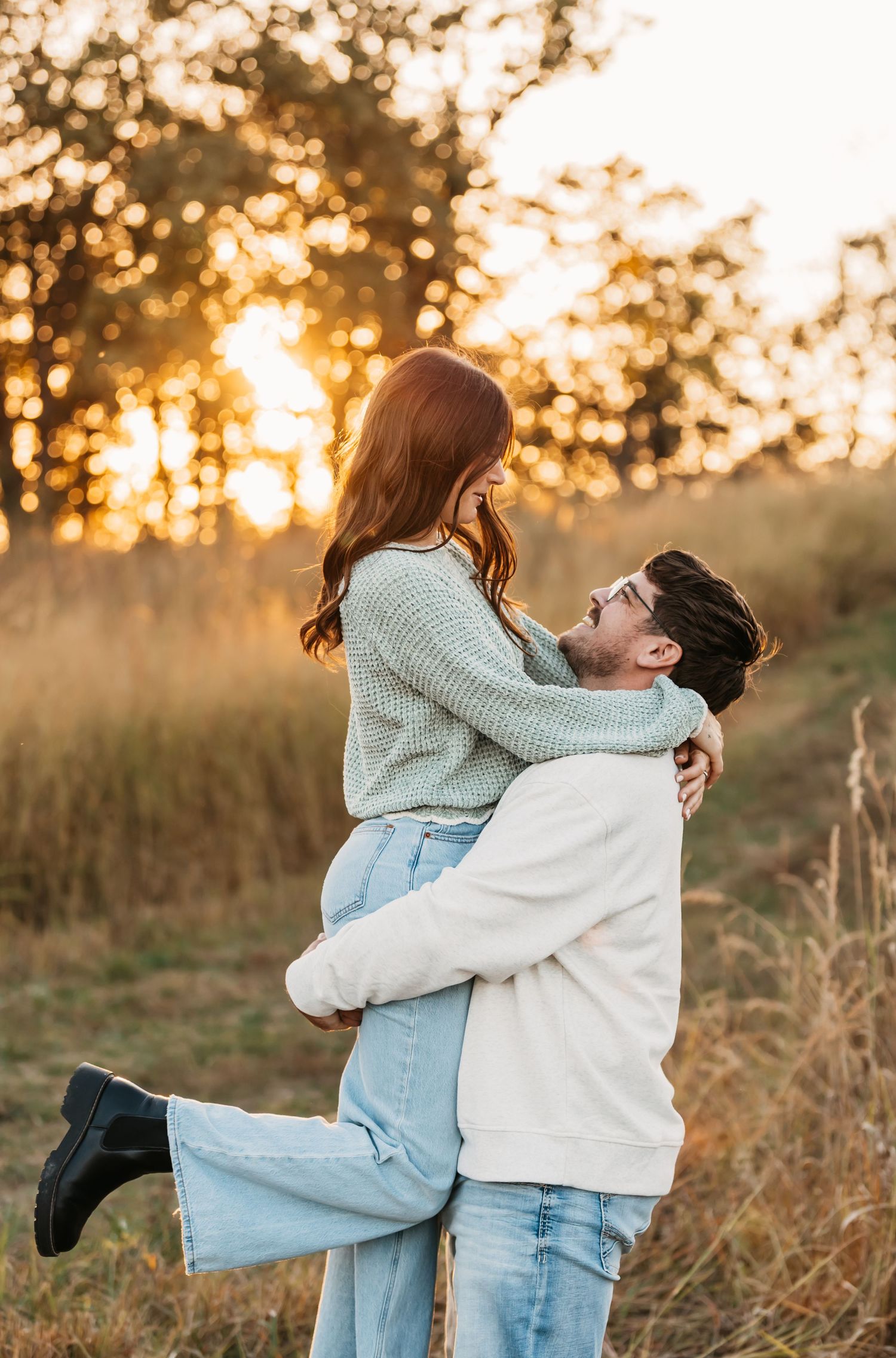 Romantic couple embracing in a golden sunset field with bokeh lighting effects in the background.