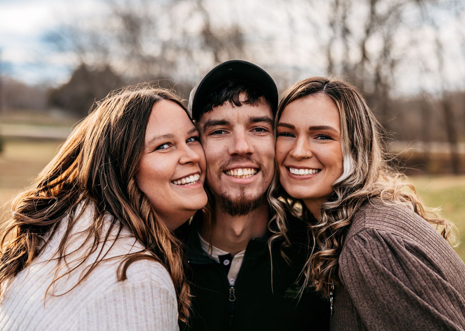 Joyful outdoor family portrait with people embracing and smiling in warm sunlight.