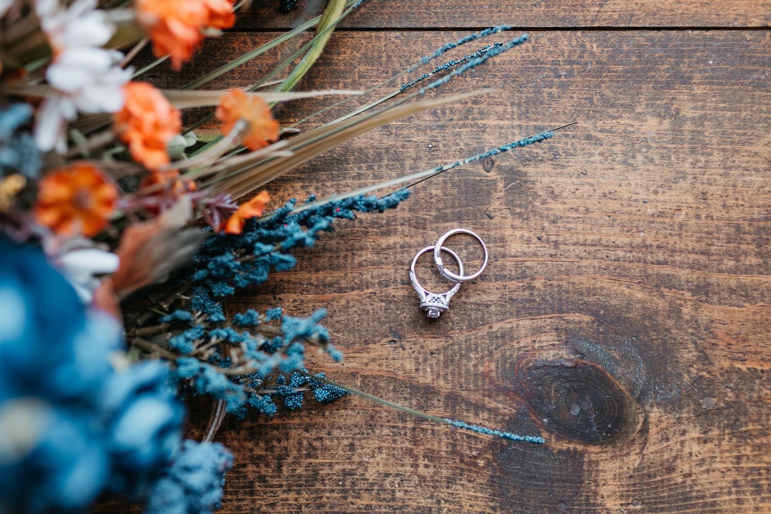Wedding rings and floral decorations arranged on a wooden surface.