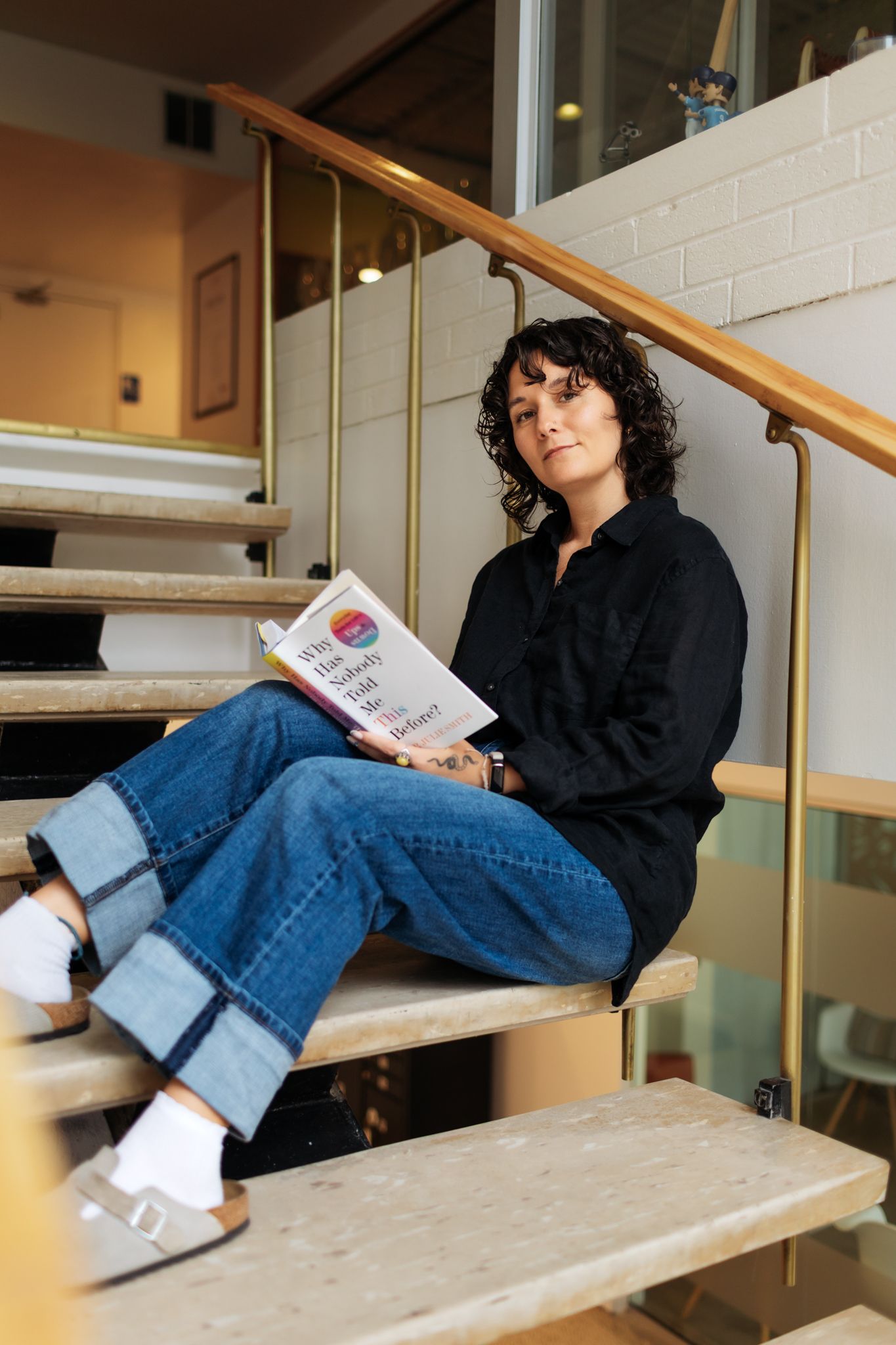 Person in black jacket and jeans relaxing on stairs while reading.
