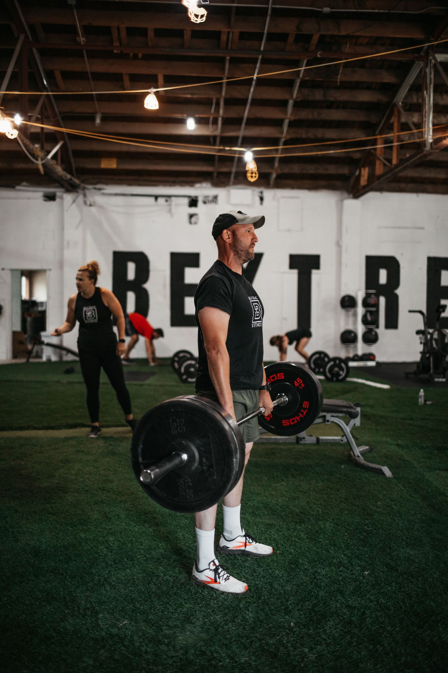 Athletes performing deadlifts with barbells on artificial turf in a warehouse gym.