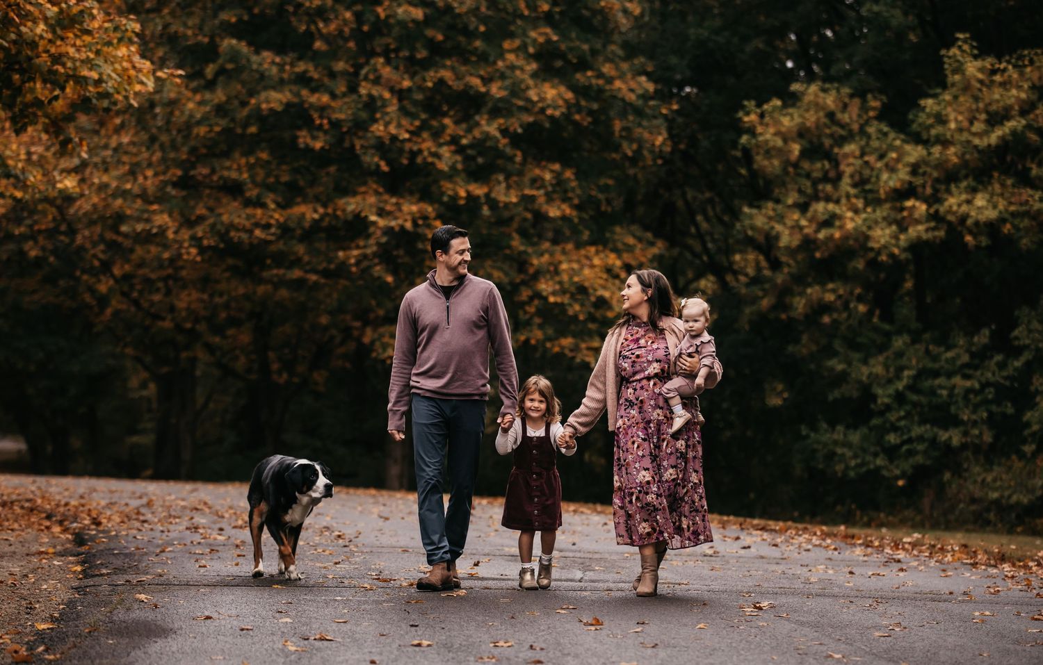 A family walking together on an autumn path surrounded by orange and brown fall foliage.