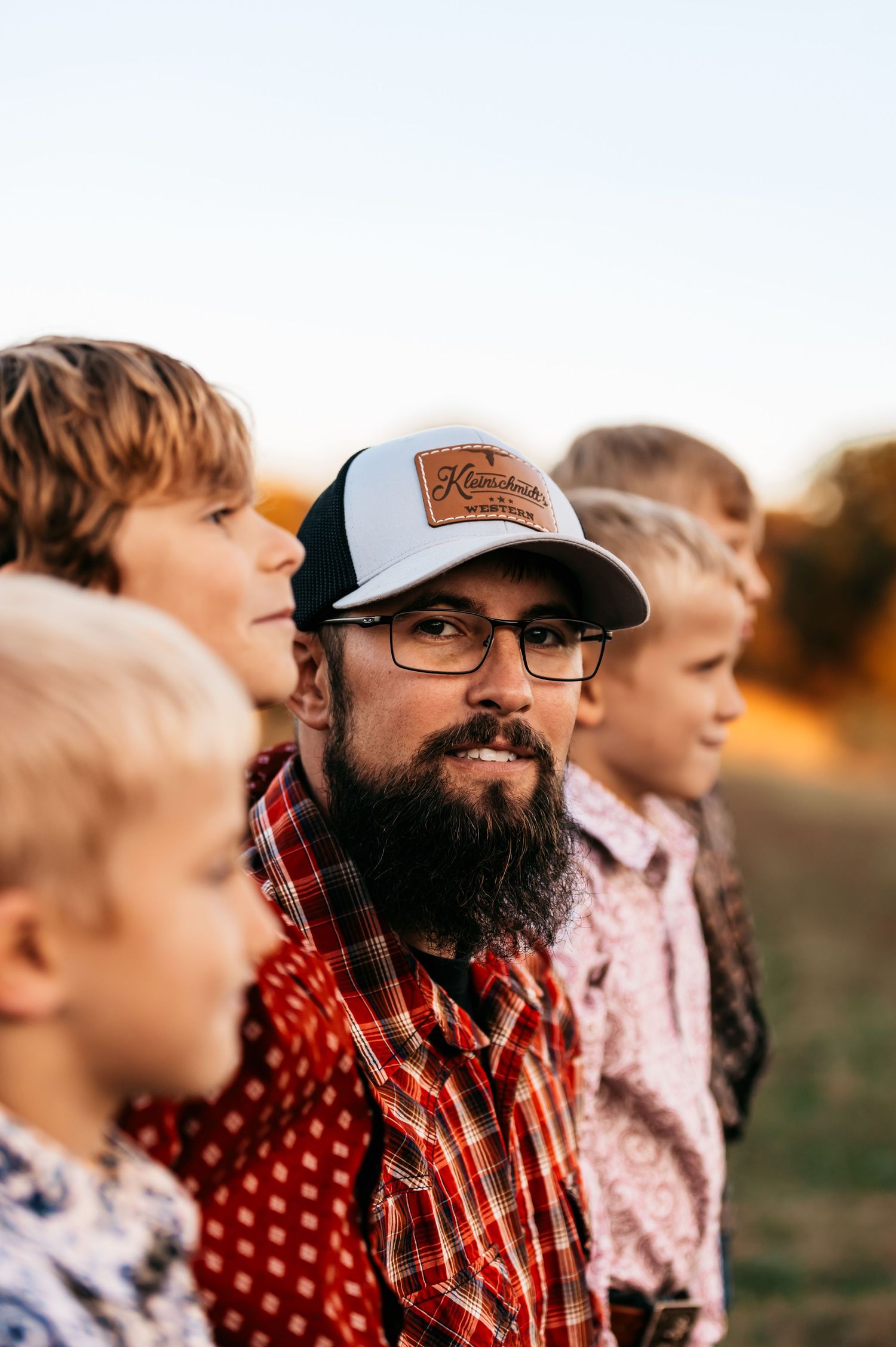 A casual outdoor portrait of a dad and sons, dad is facing the camera smiling.