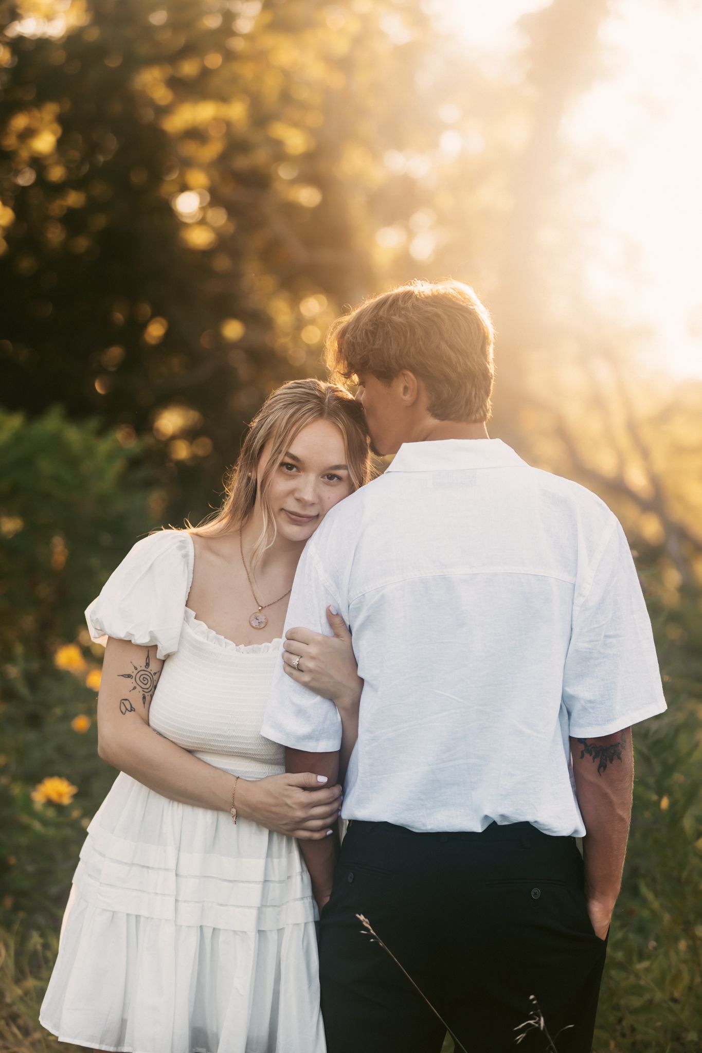 Tender moment shared between couple in white outfits against sunset-lit nature backdrop.