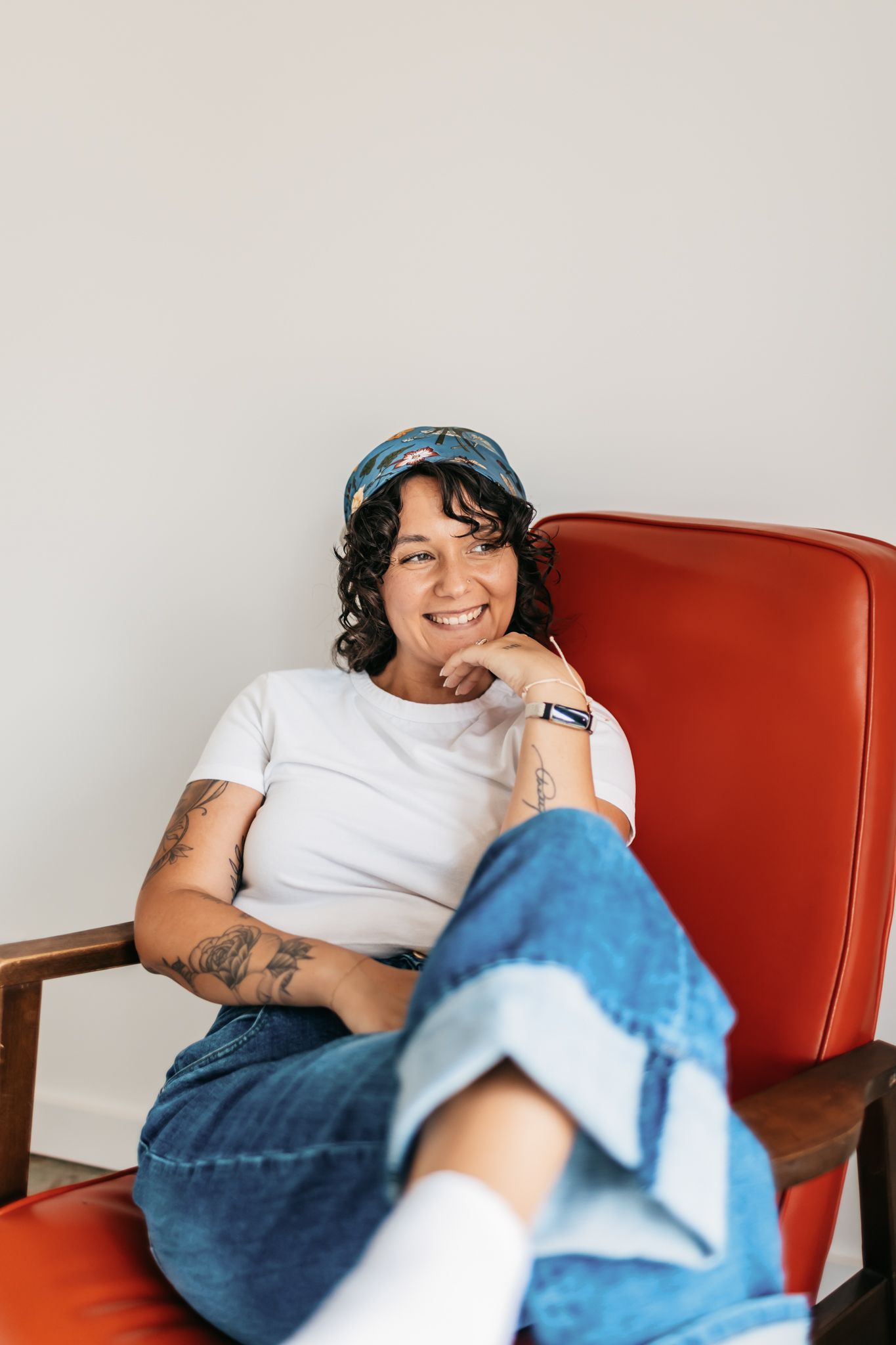 Relaxed lifestyle portrait in a red vintage chair wearing denim and a white t-shirt.