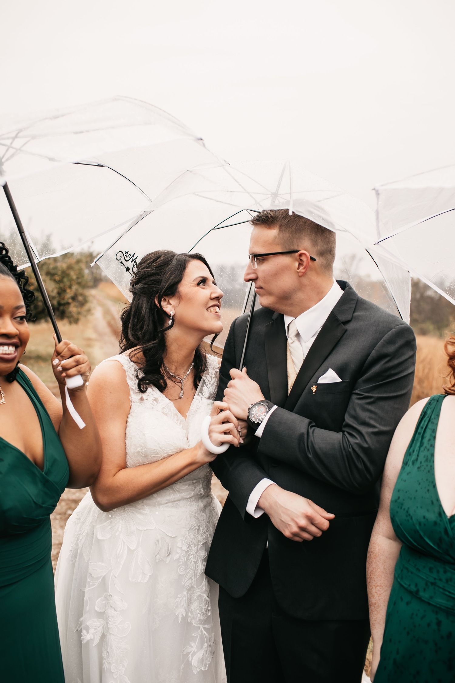 Wedding party shares laughs while holding clear umbrellas during an outdoor photoshoot.