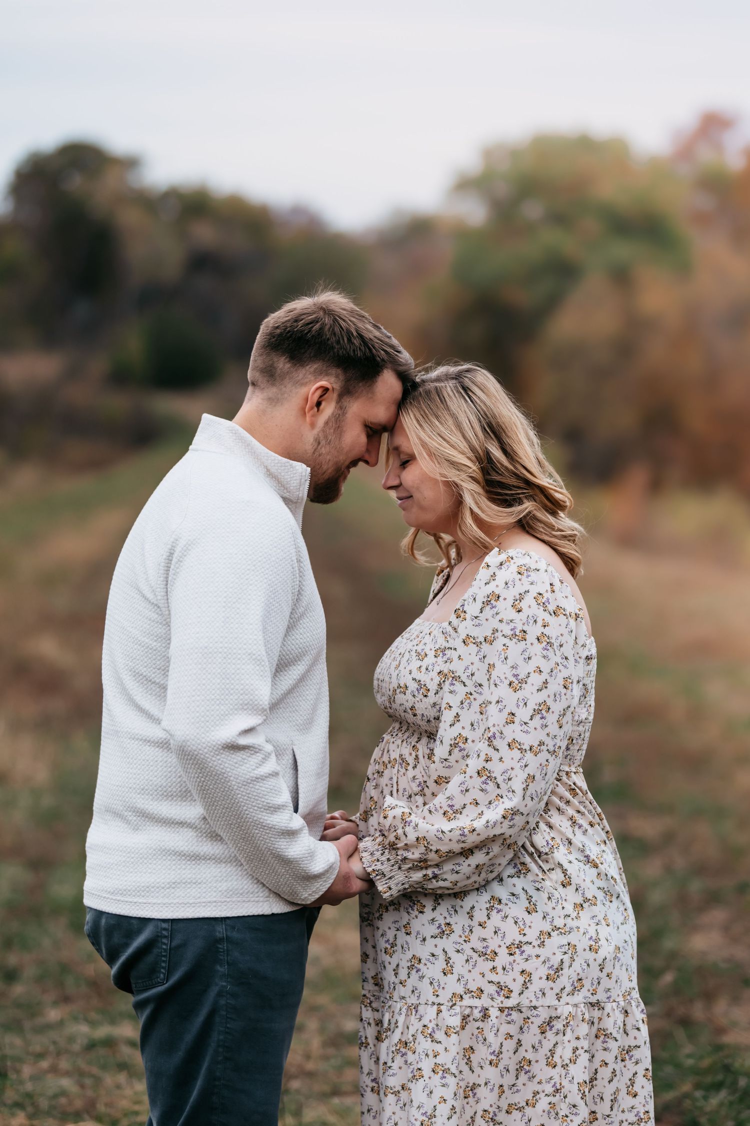 Romantic couple embracing in a field during autumn wearing white and floral outfits.