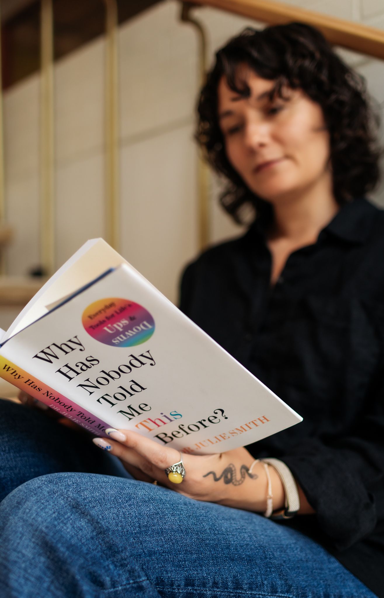 A reader holds the book 'Why Has Nobody Told Me This Before?' while relaxing in casual attire.