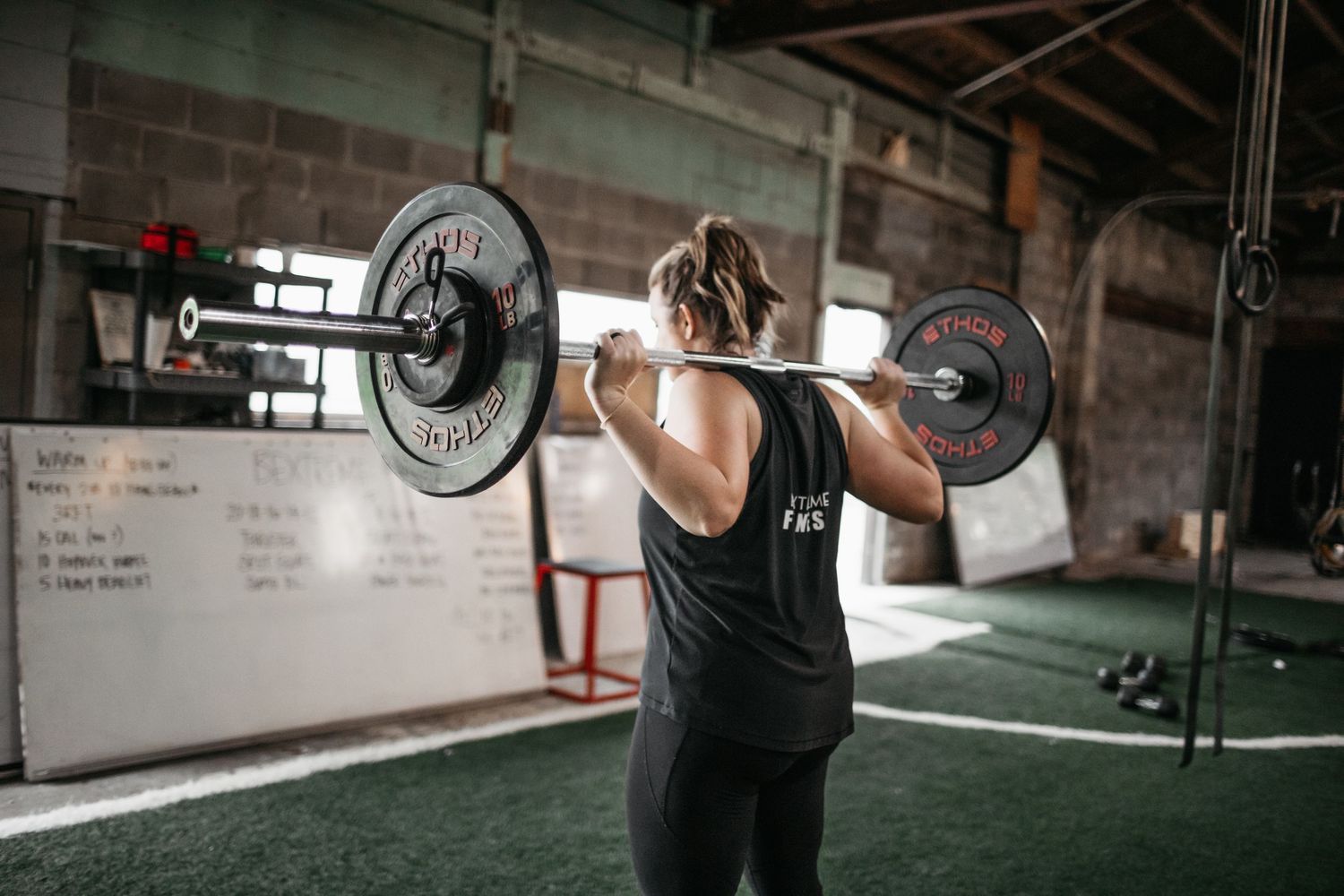 Athletes performing synchronized barbell exercises in a brick-walled fitness facility.
