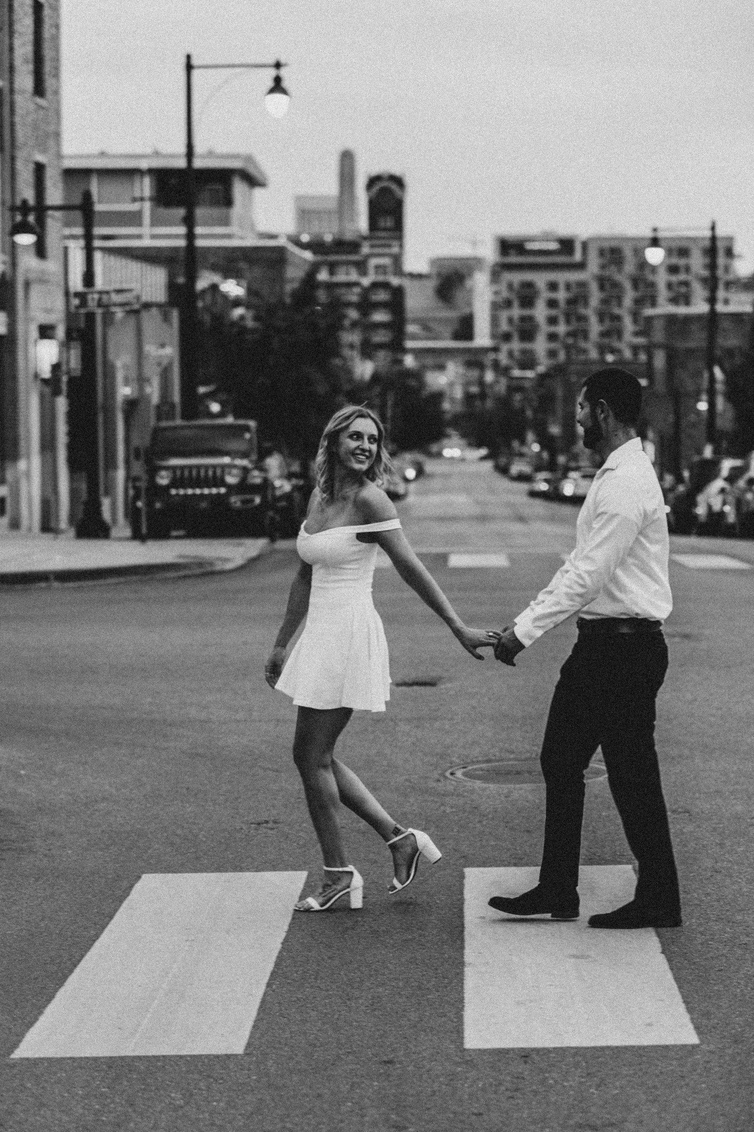 Playful couple recreating Beatles Abbey Road crossing pose in urban setting.