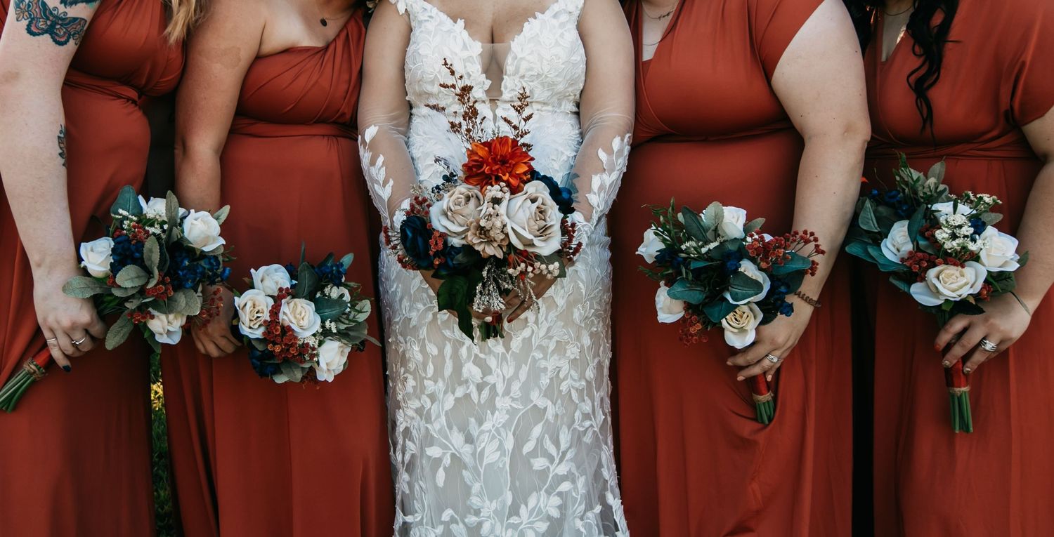 Wedding party holding floral bouquets against burgundy dresses.