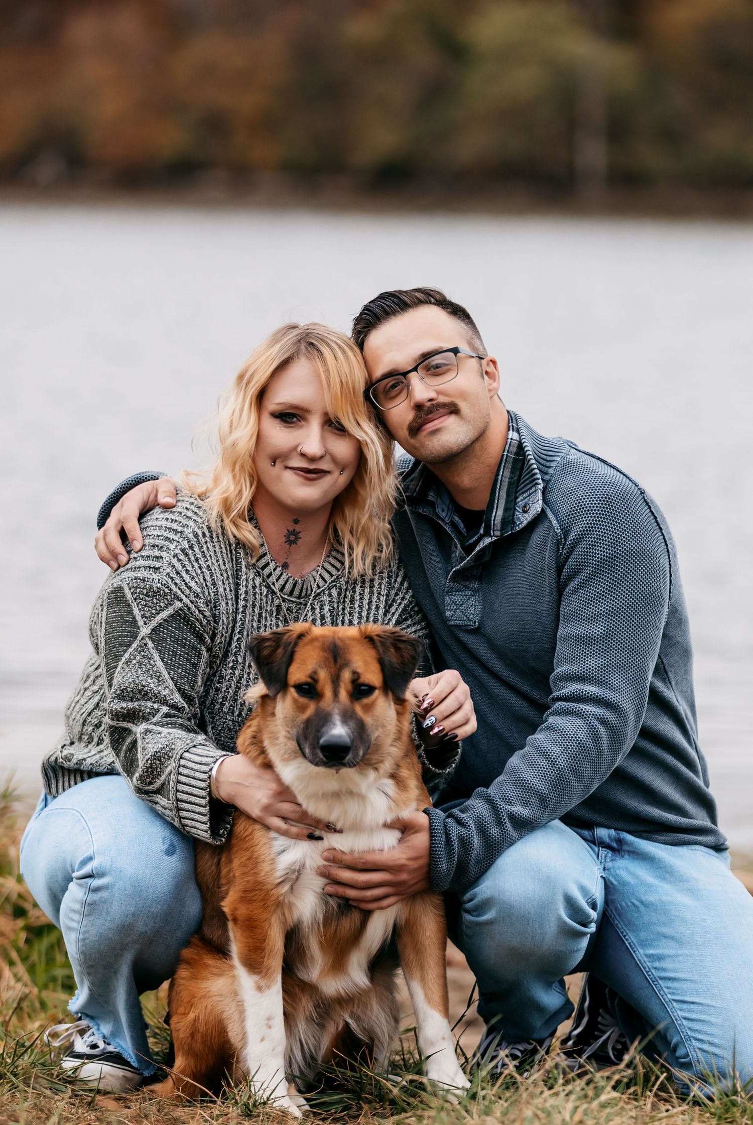 Couple sitting on grass with their brown and white dog during an outdoor photo session.