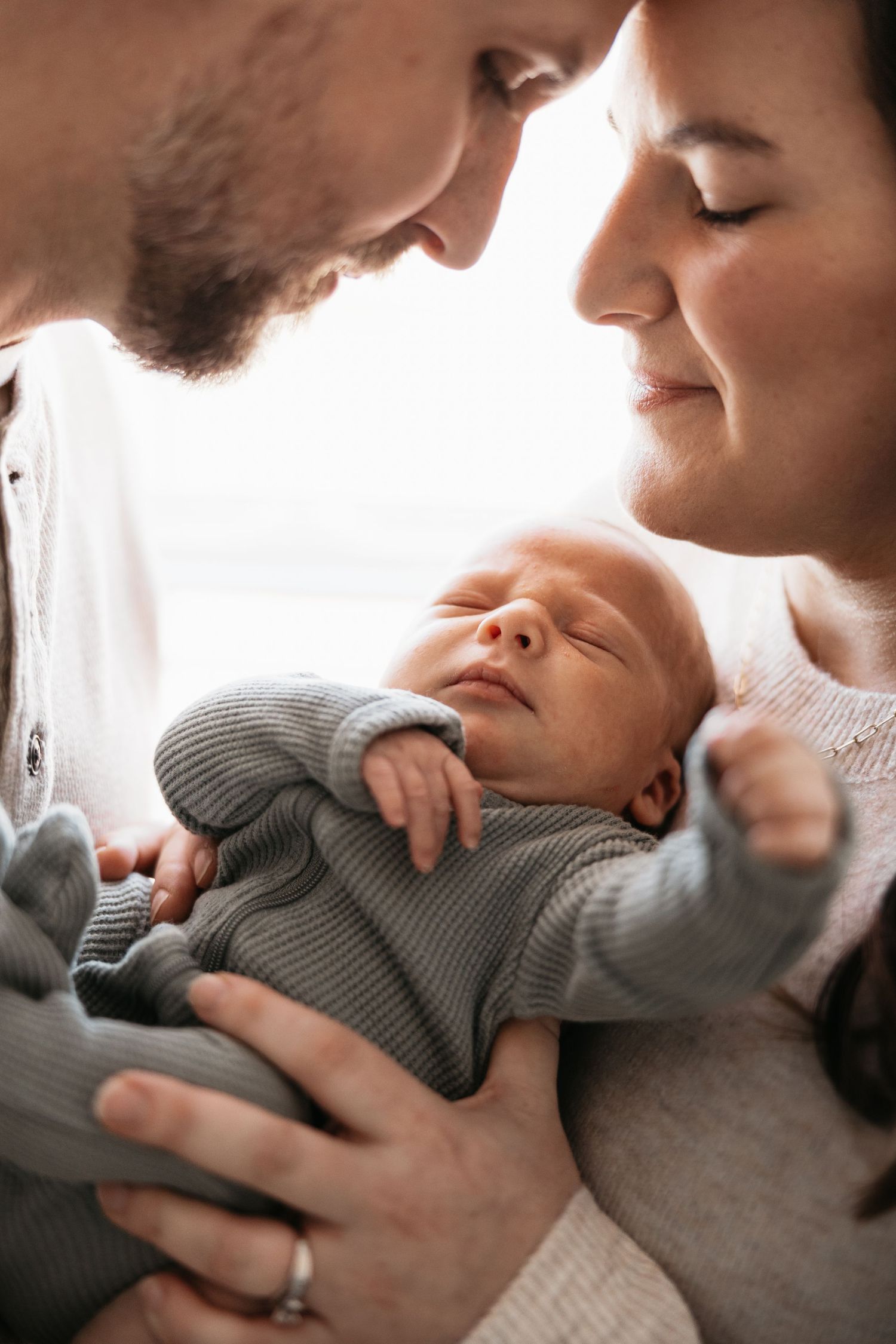 Intimate close-up of parents tenderly cradling newborn baby in gray outfit.
