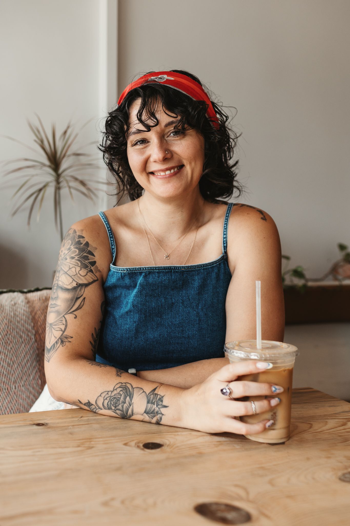 A casual coffee shop scene with a red cap, denim top, and visible tattoos.