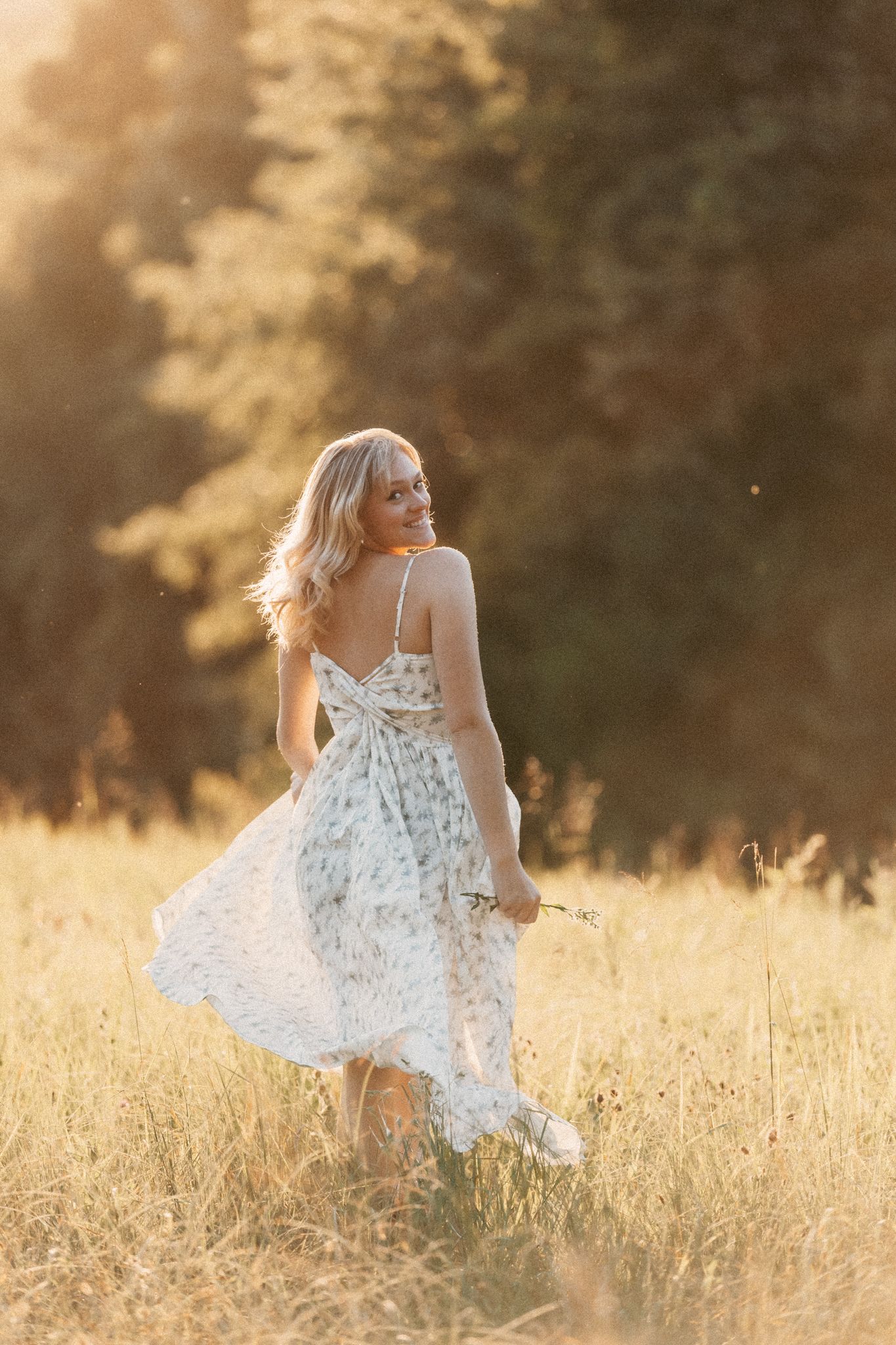 Young child in white dress twirling playfully through a sunlit golden field at sunset.