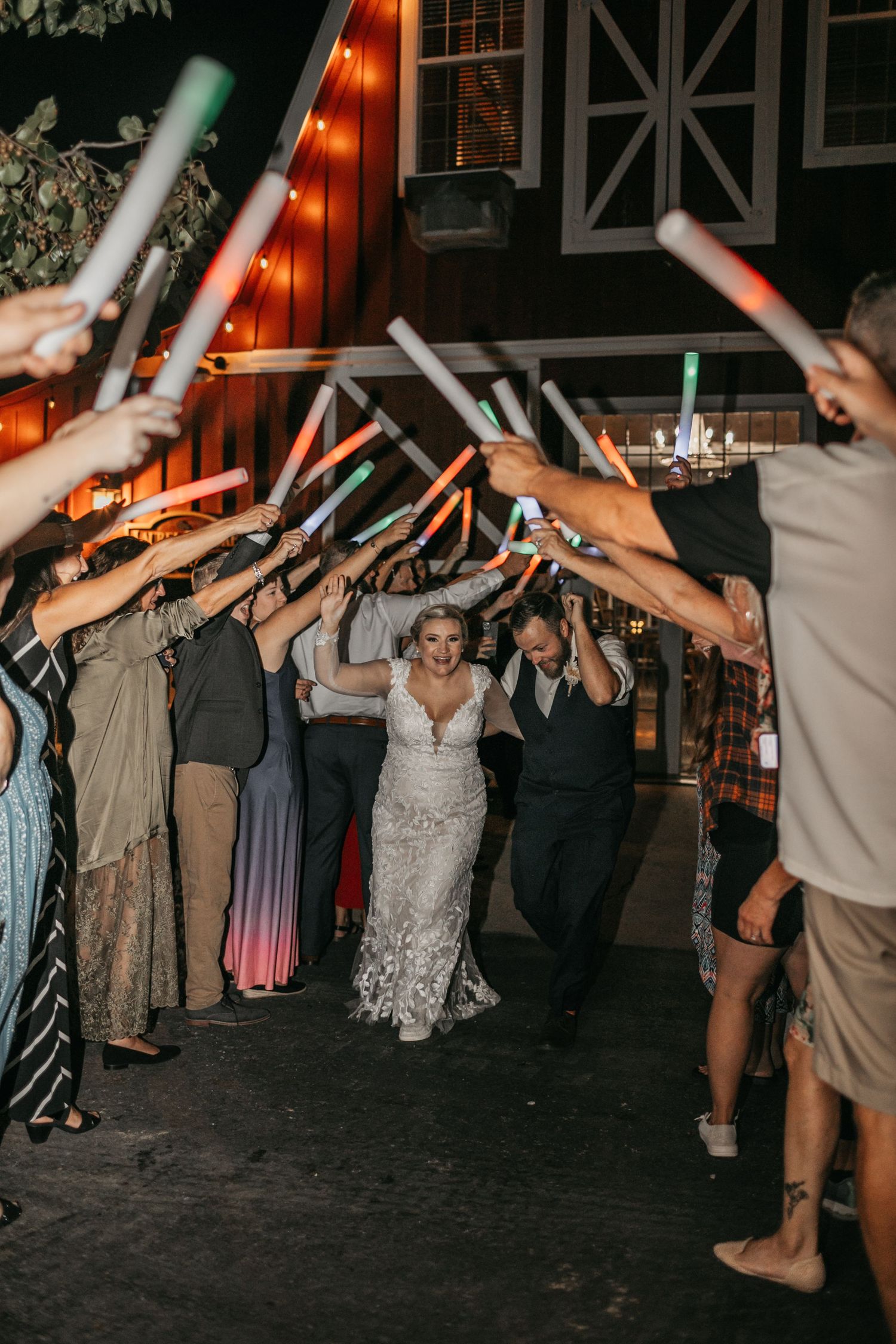 Wedding guests forming a tunnel with light-up wands during evening celebration.