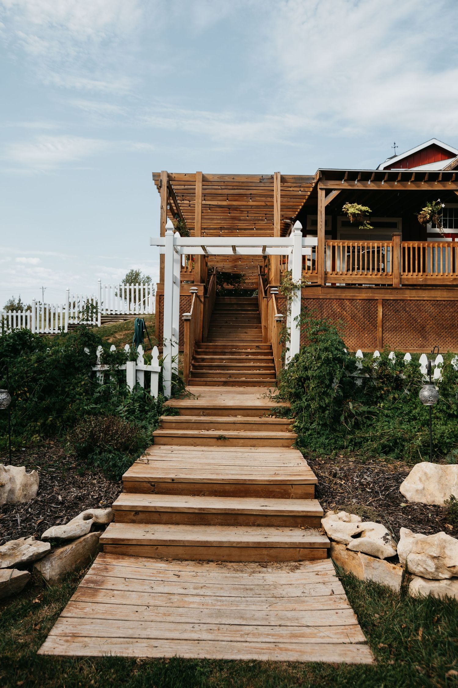 Wooden deck with white picket fence and stairs leading to a rustic wedding venue.