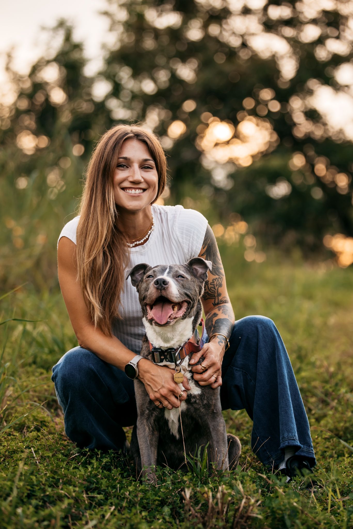 Happy grey pit bull dog and owner posing together in sunny field.