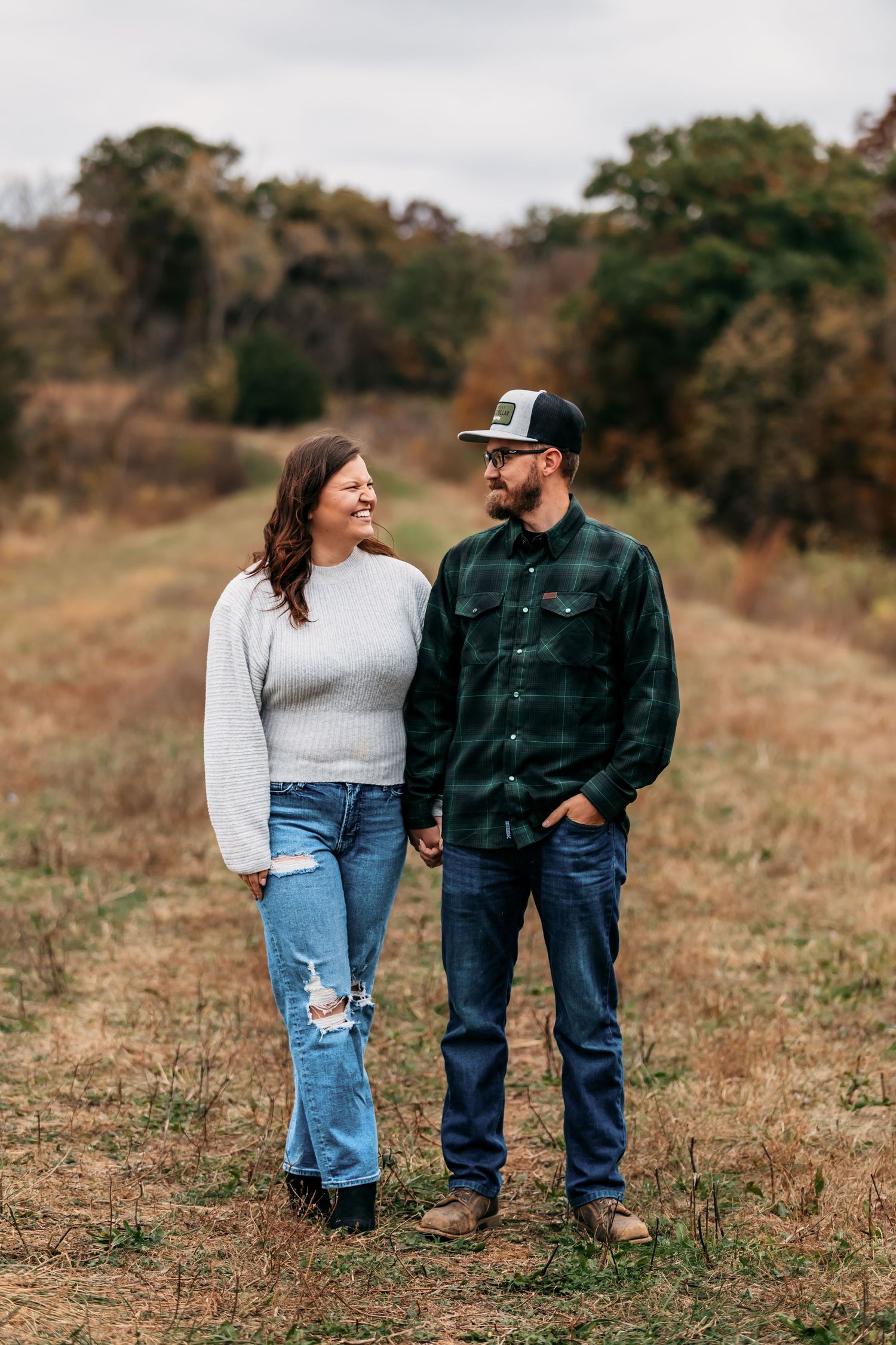 A couple walks hand in hand through a golden autumn field wearing casual attire.