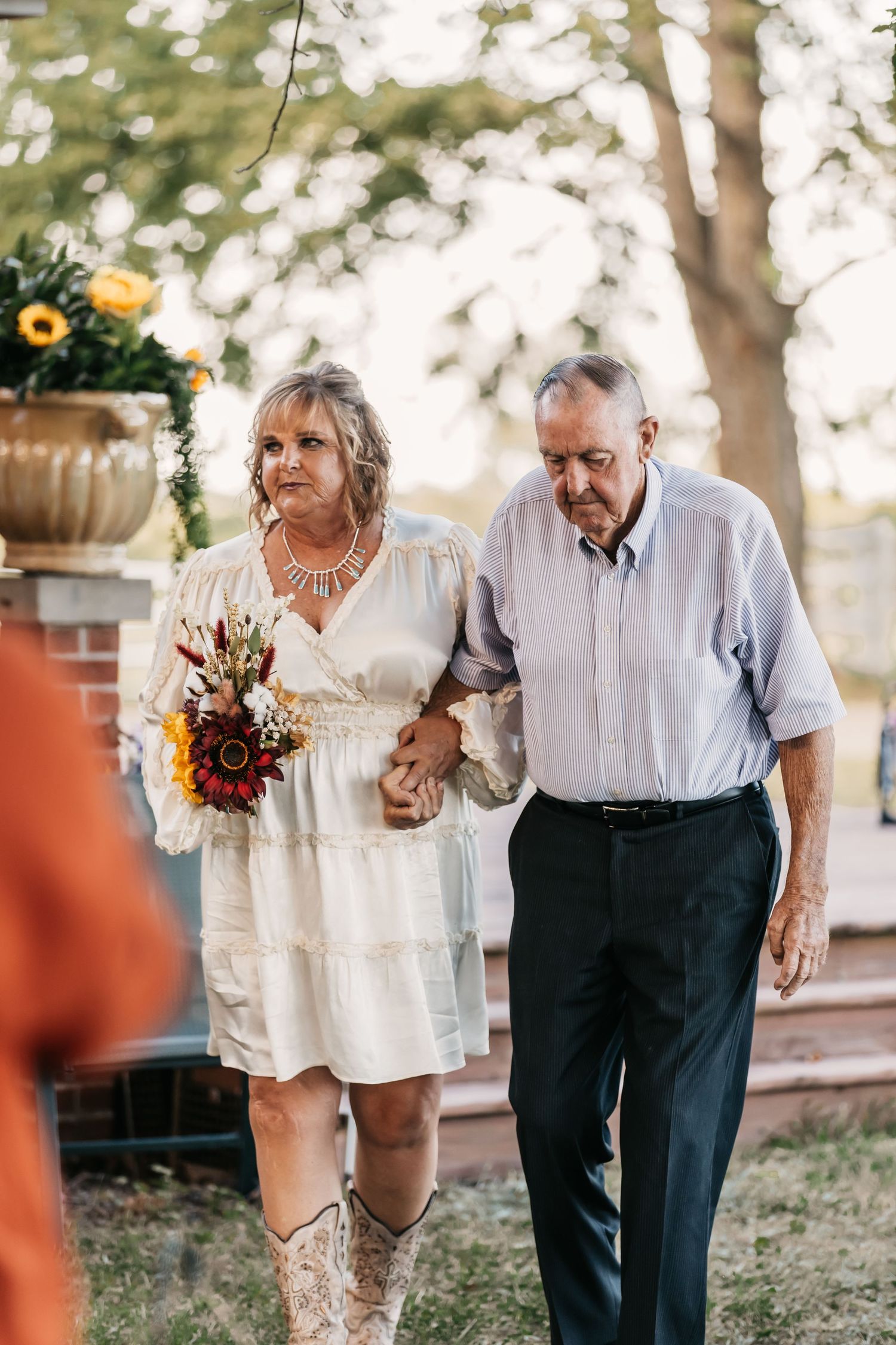 Elderly couple walking together outdoors holding hands with sunflowers in a romantic moment.