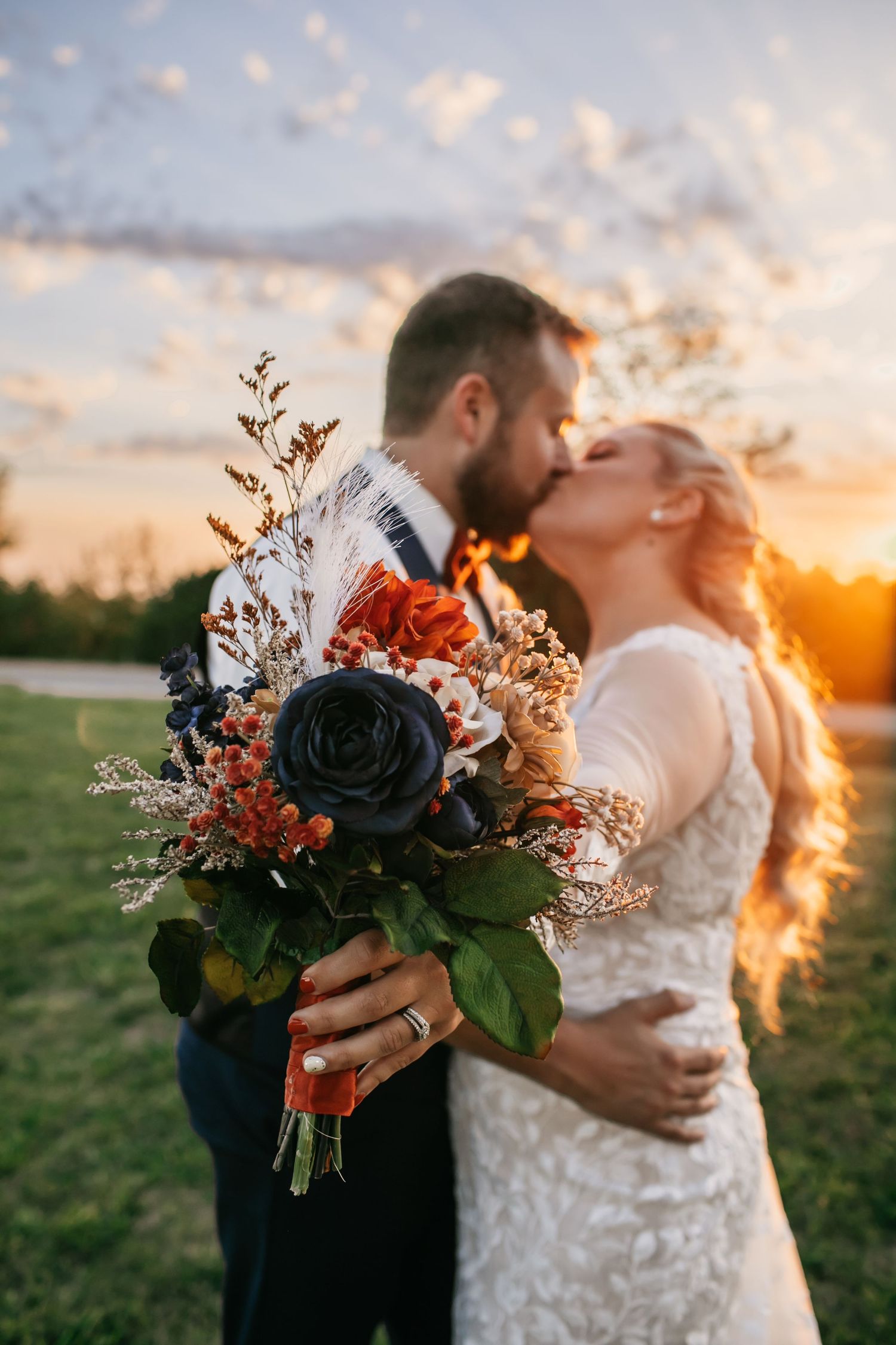 Wedding bouquet with navy and orange flowers silhouetted against sunset sky.