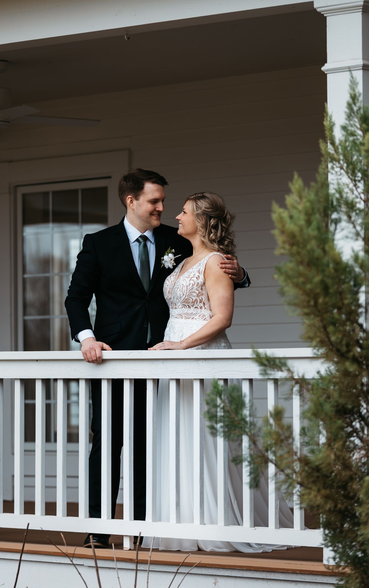 Newlyweds share tender moments on a white porch railing at their wedding venue.