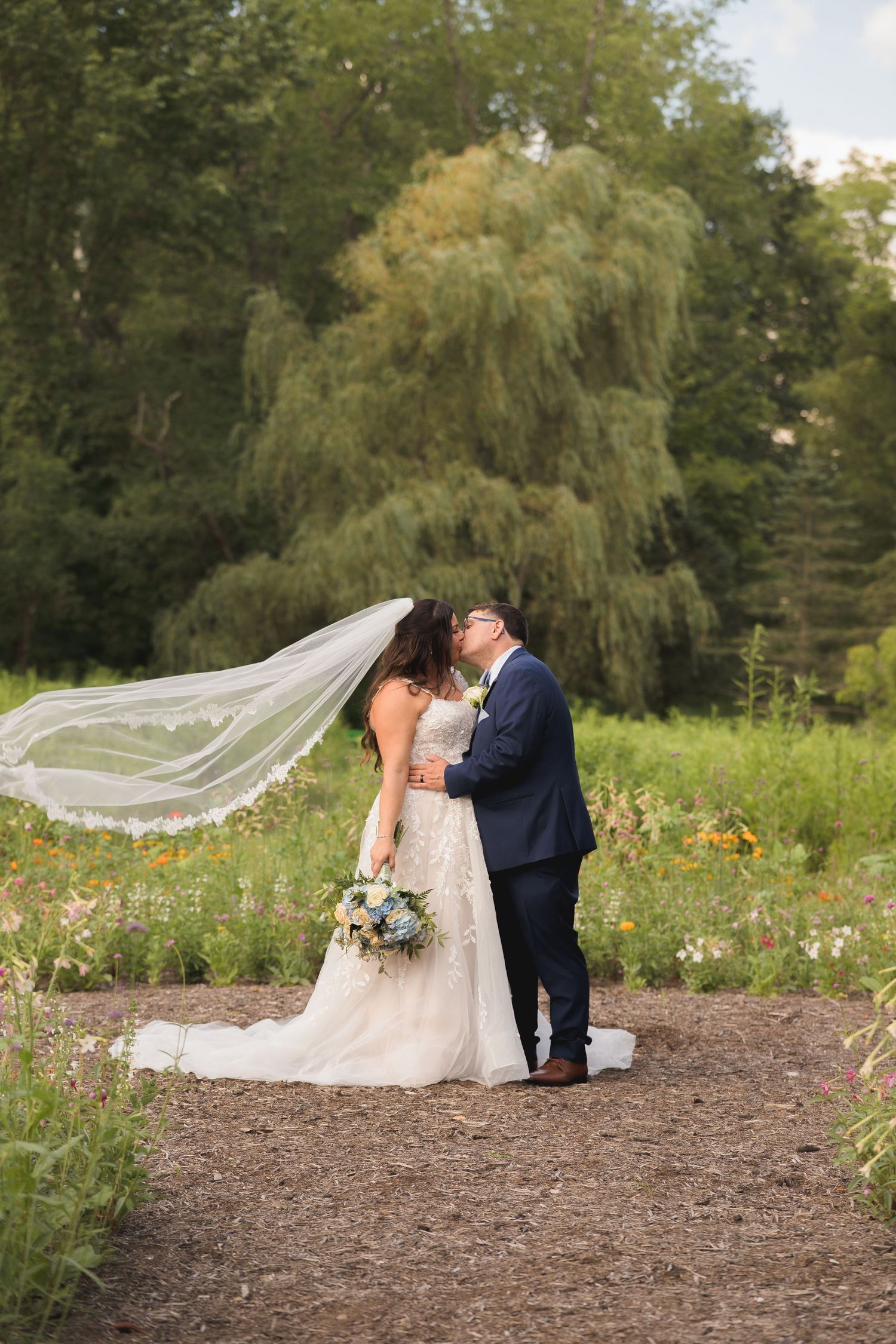 Couple sharing romantic moment in garden with flowing veil and wildflowers.