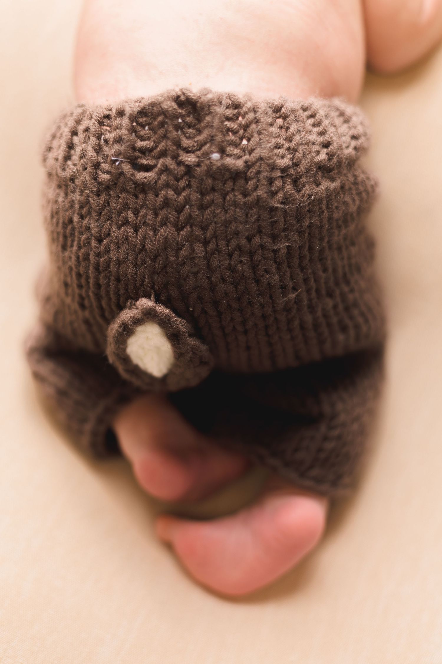 Close-up of a newborn baby foot wearing a brown knitted sock with a small button detail.